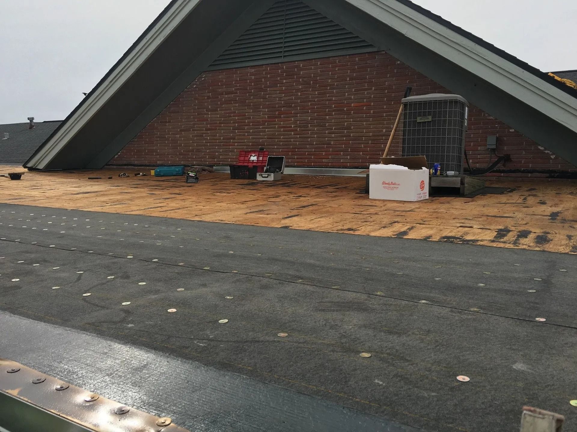 Roof under construction with exposed plywood, red toolboxes, and a white box on the roof edge.