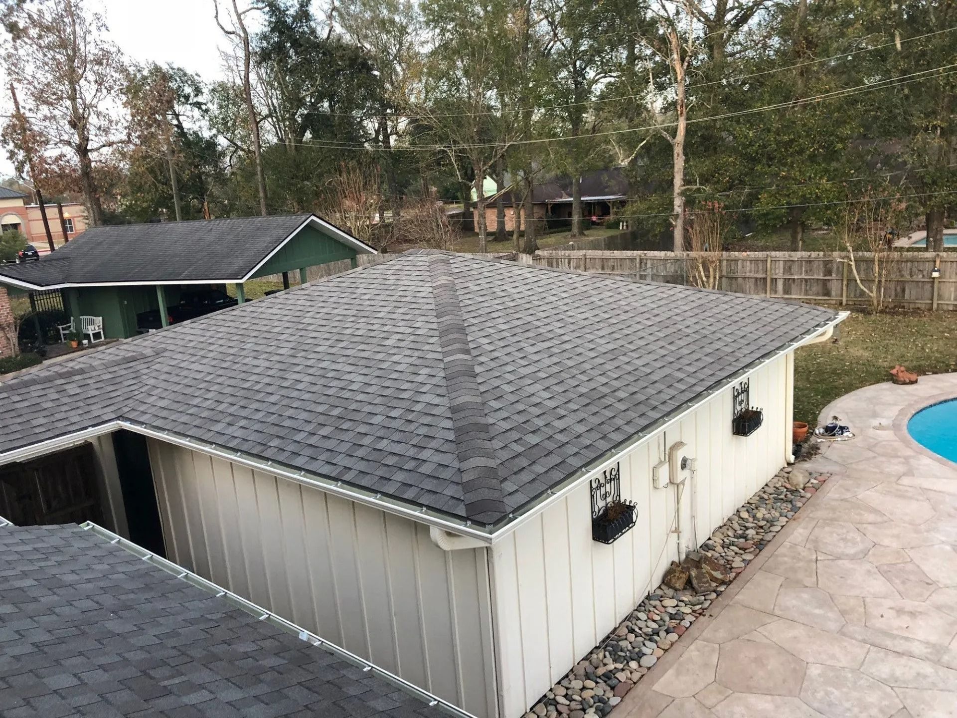 Backyard view of a gray-roofed shed beside a swimming pool and wooden fence