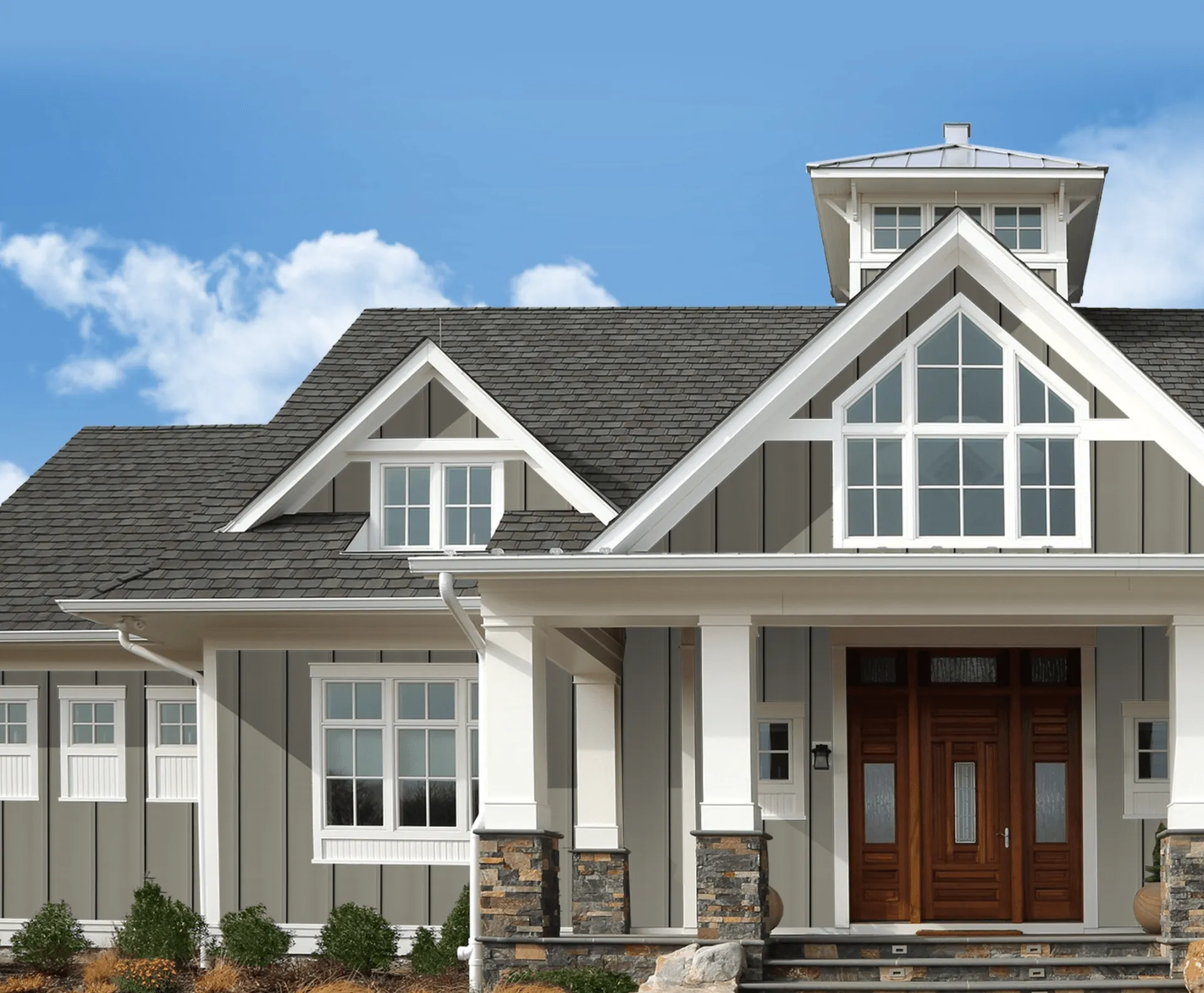 Gray suburban house with white trim, dark shingle roof, and a front porch with wooden double doors.
