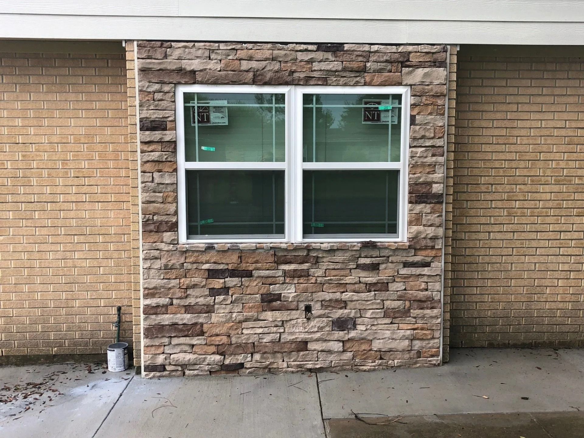 Exterior brick wall with a white-framed double window and concrete walkway.