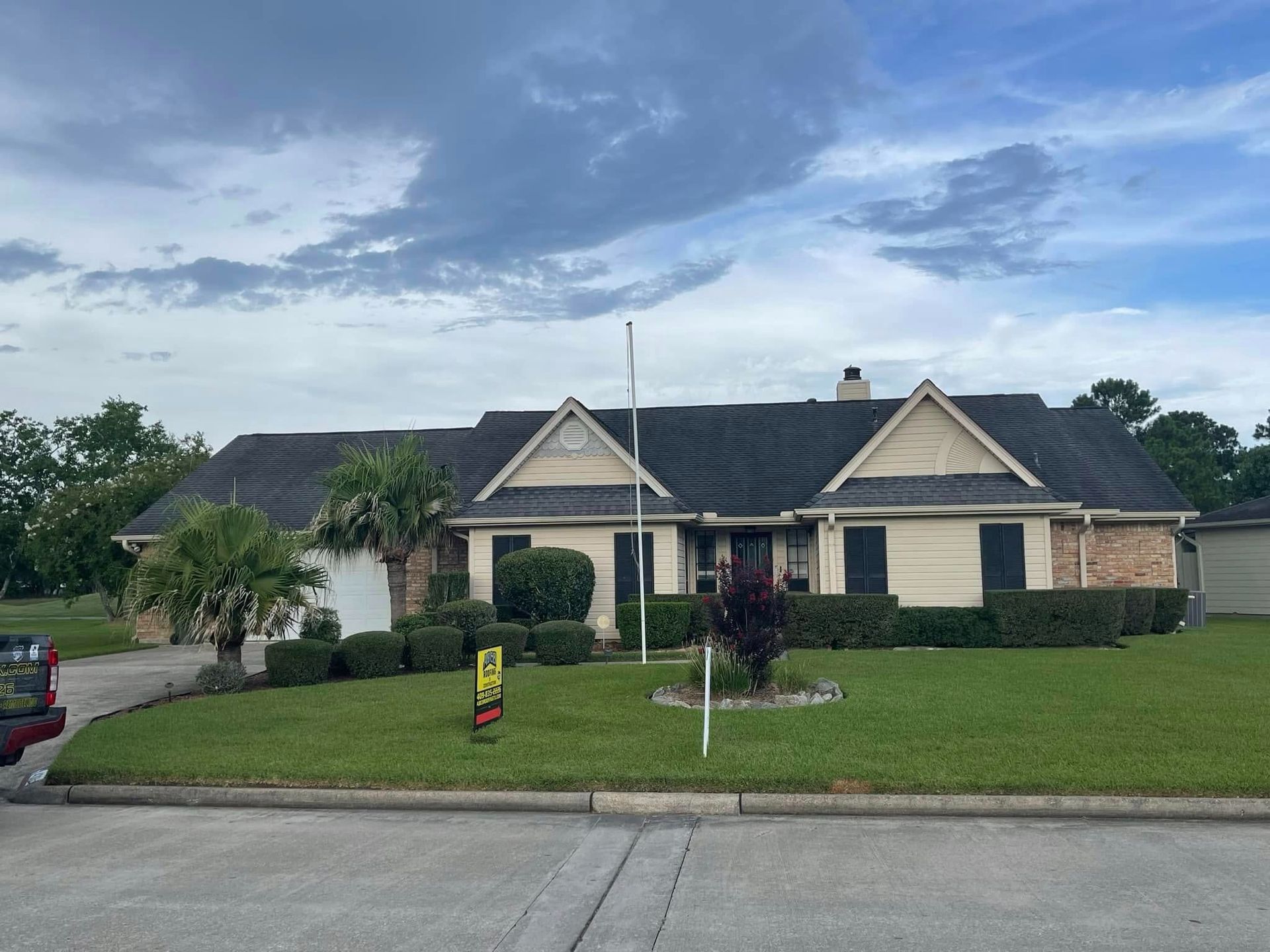 Suburban single-story stone house with manicured lawn and cloudy evening sky