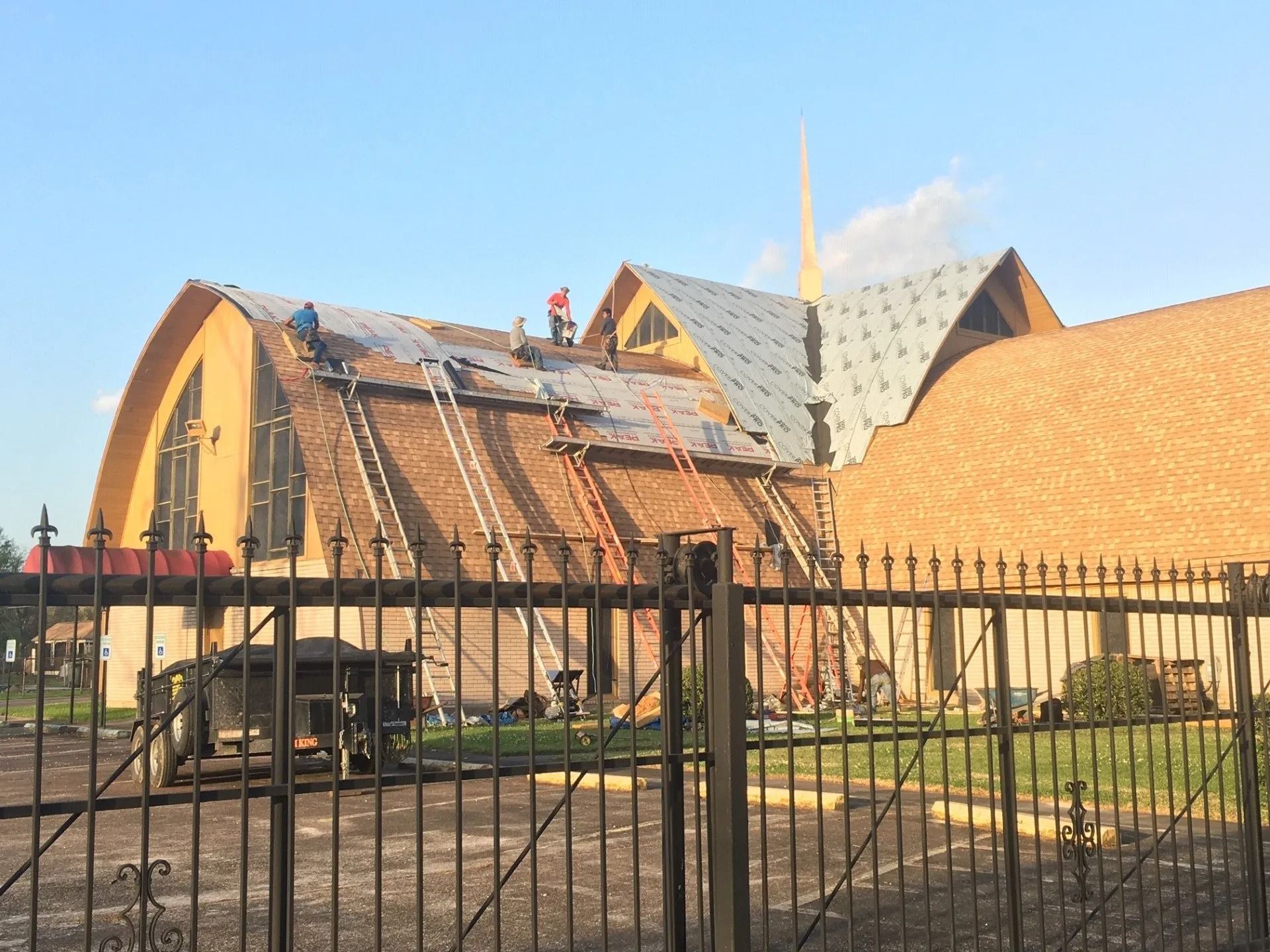 Damaged church roof with exposed beams behind a black metal fence under a clear sky