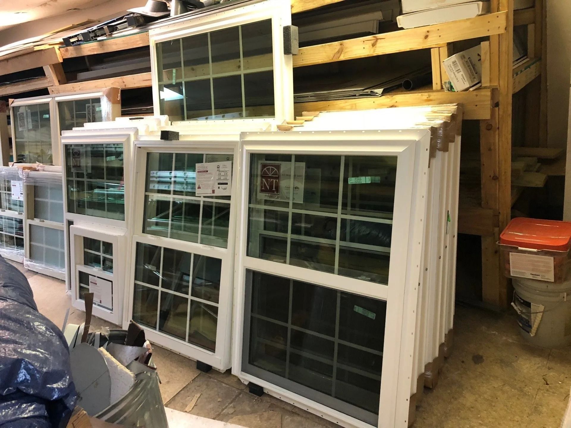 Stacked white replacement windows in a workshop or storage area.