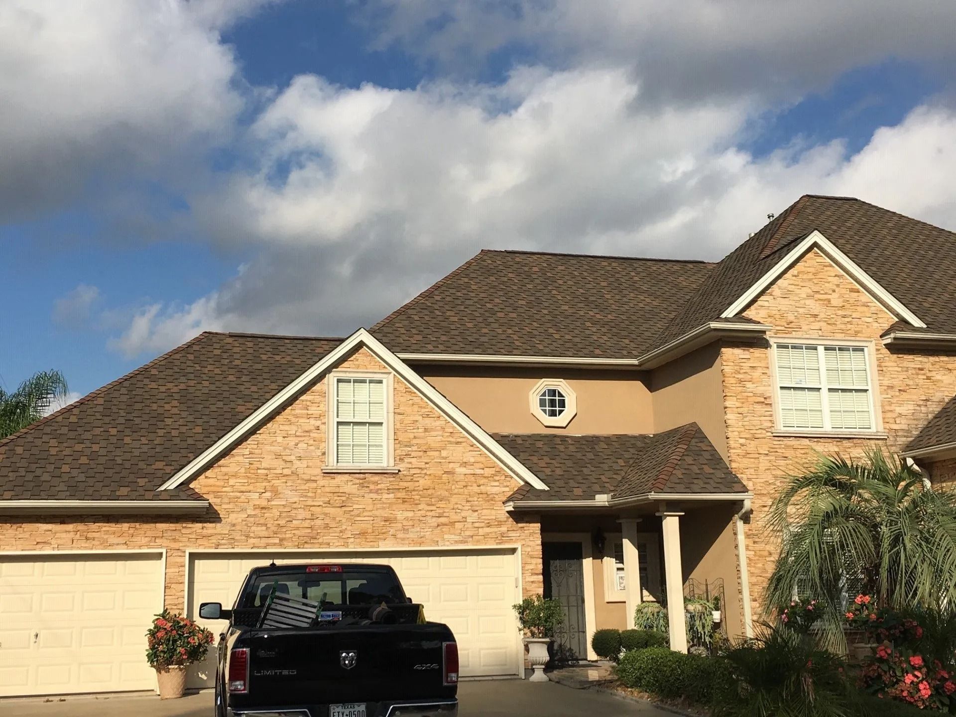 Two-story tan brick house with a black pickup in the driveway under a partly cloudy sky