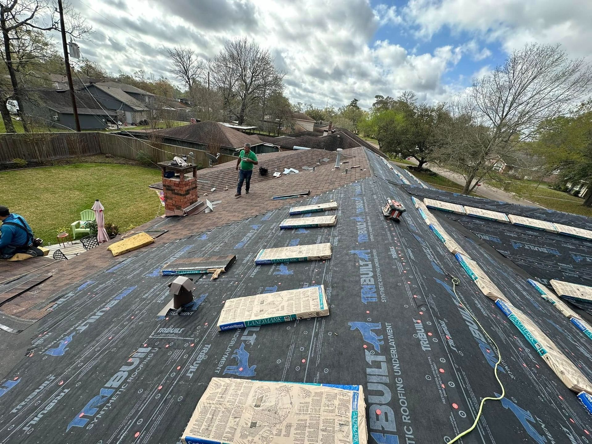 Workers installing roofing underlayment on a sloped roof, with tools and materials spread across the surface.