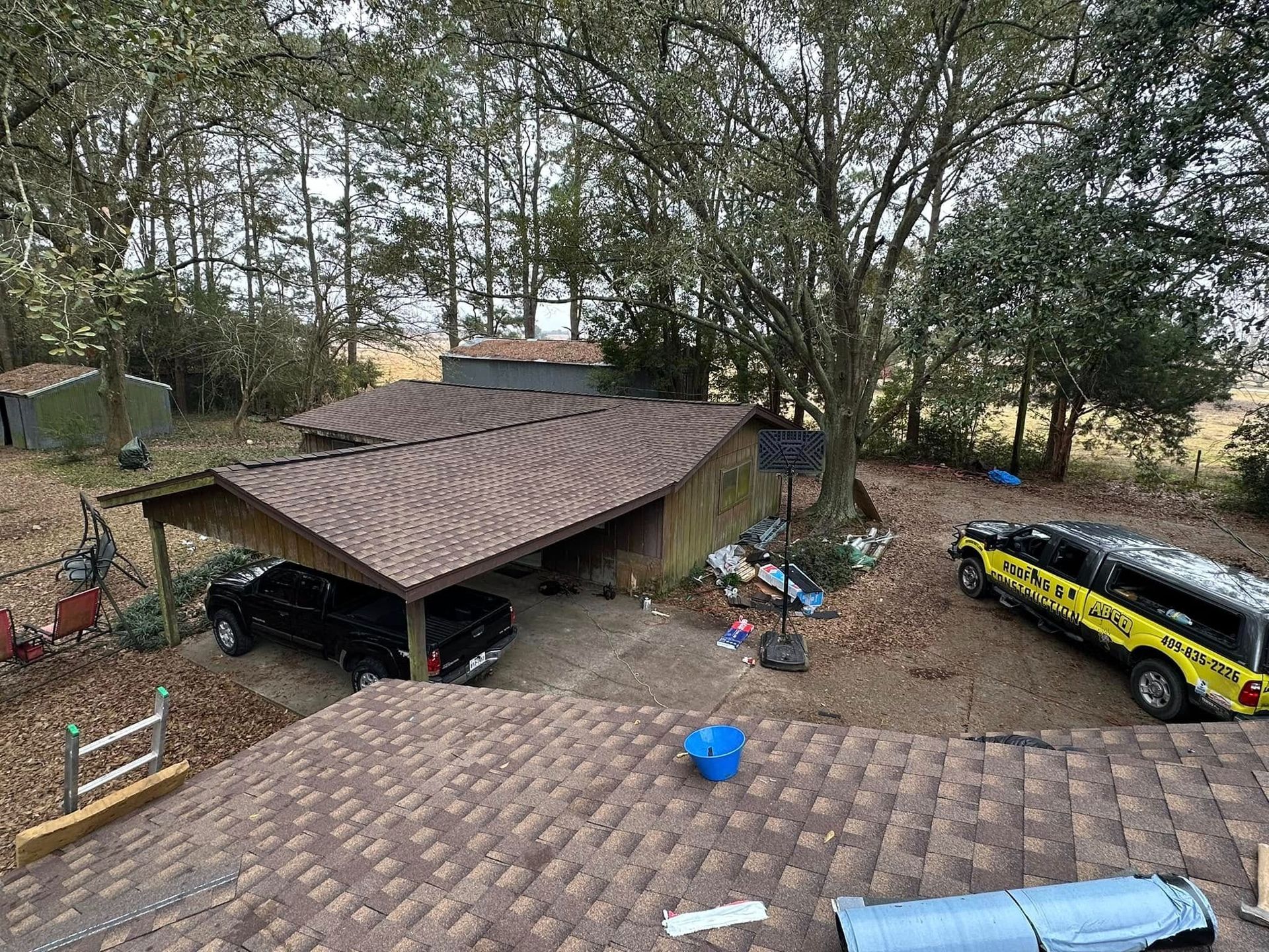 Outdoors, a shed and parked cars sit under trees; a yellow race car trailer is visible on the right.