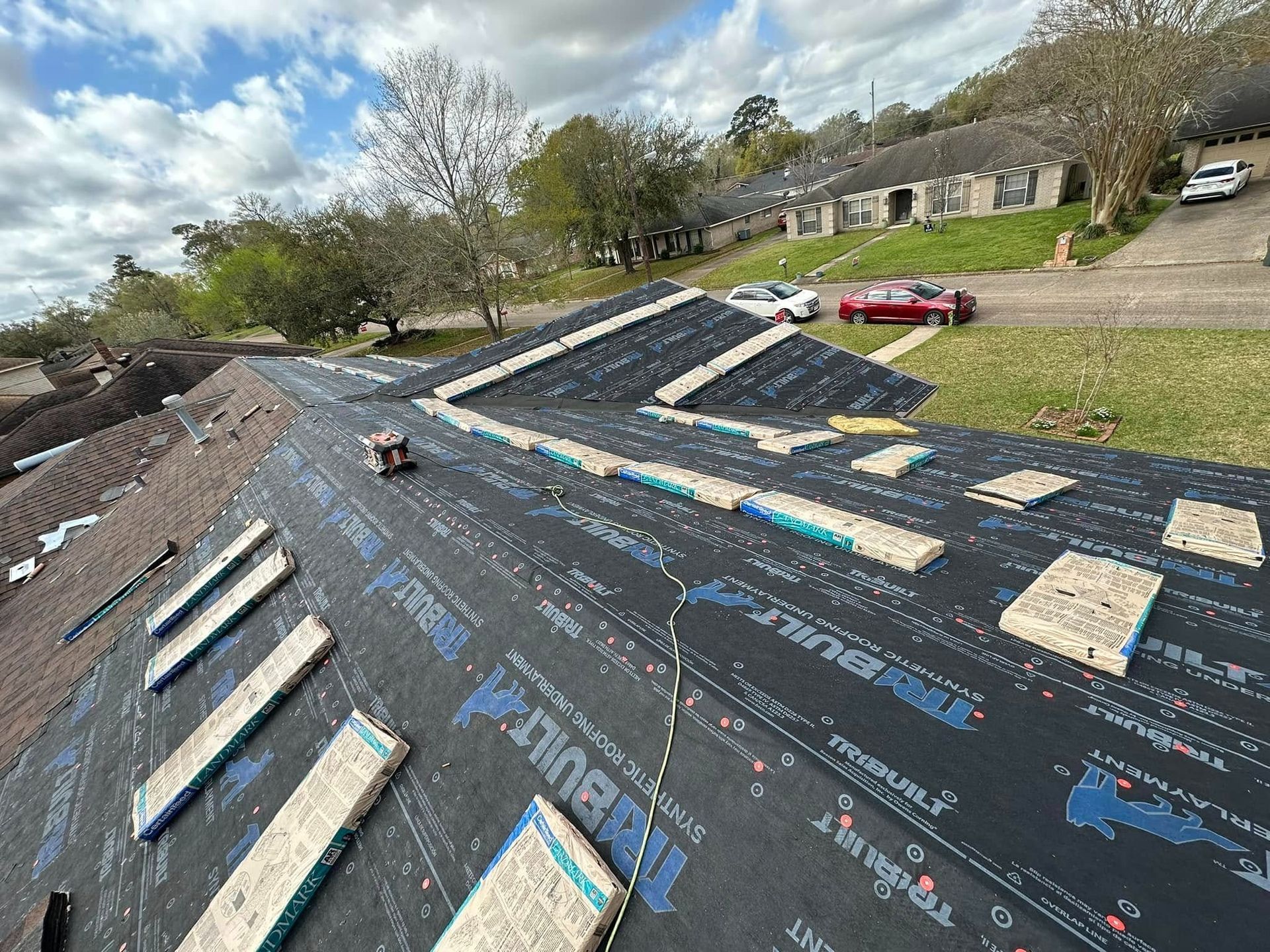 Roof under construction with black roofing felt, solar panels, and a car in the driveway below