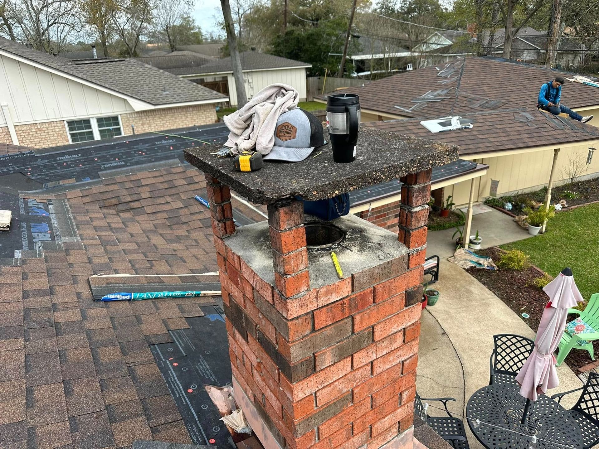 Brick chimney on a shingled roof with tools and a black bottle on top.