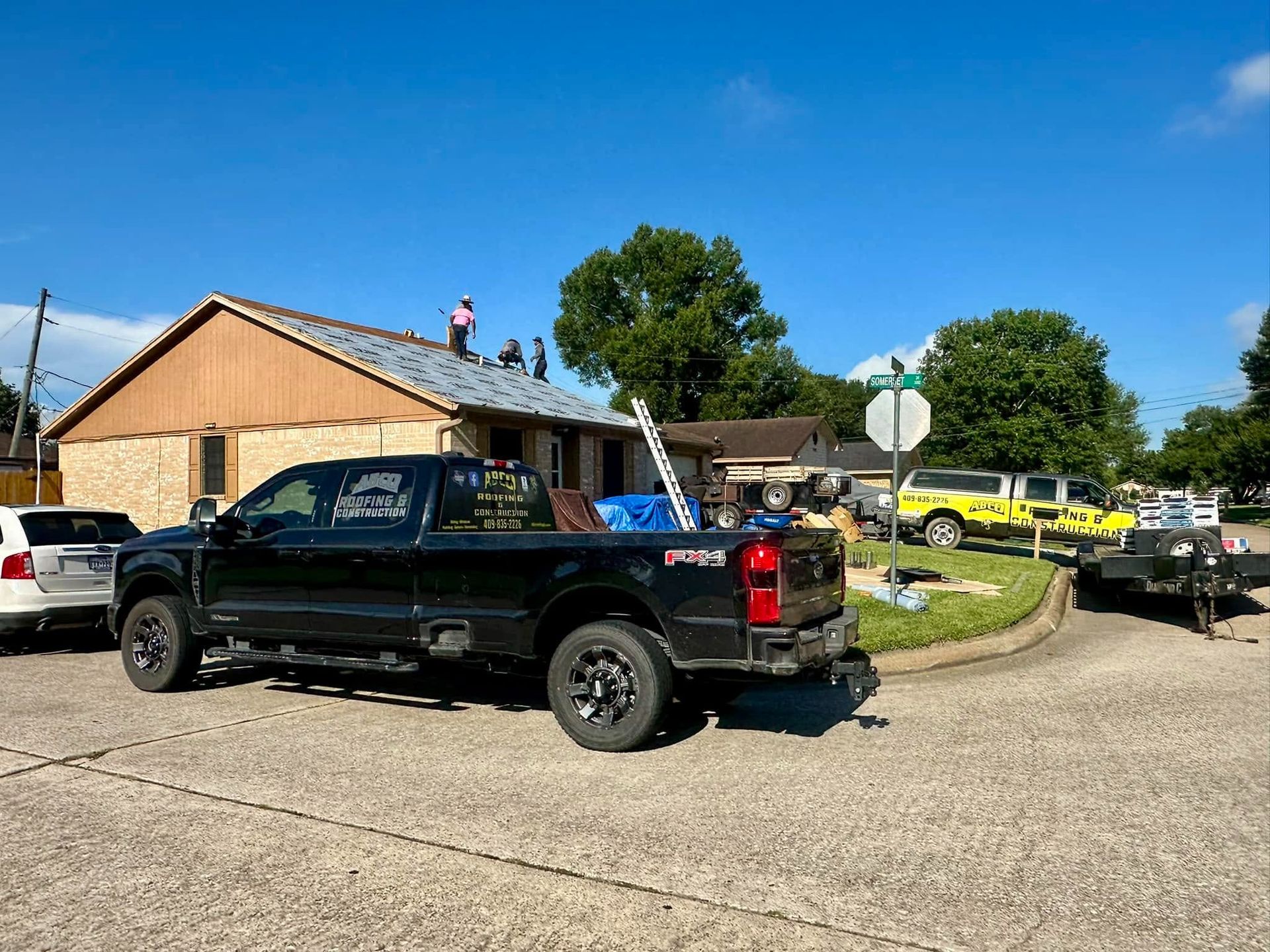 Black pickup truck parked by a house, with several yellow emergency vehicles in the background.