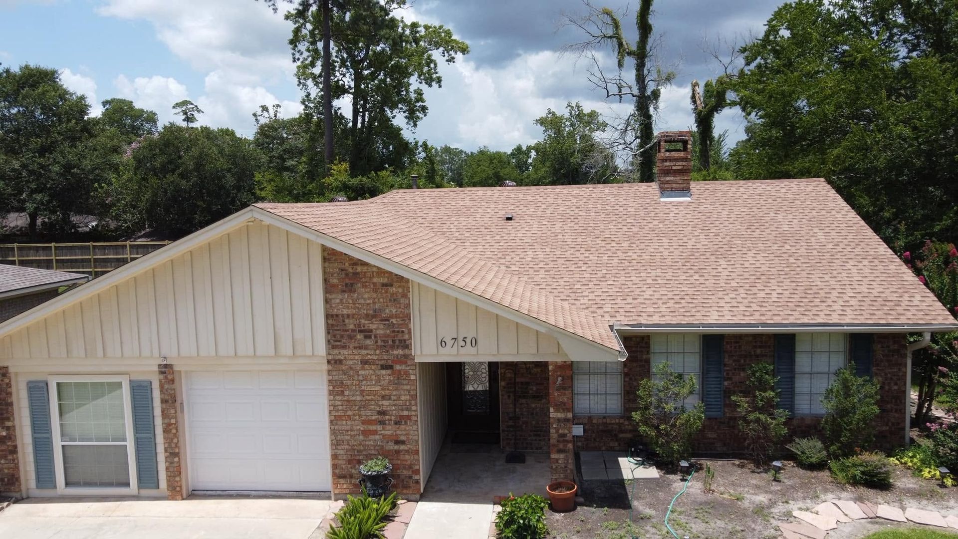 Suburban brick house with a beige roof, white garage, and front porch surrounded by trees