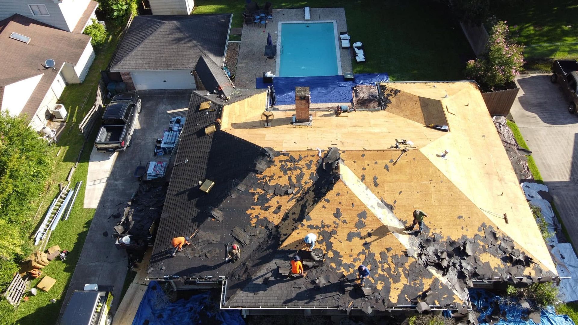 Aerial view of a house roof under repair, with exposed black and yellow roofing and a backyard pool.