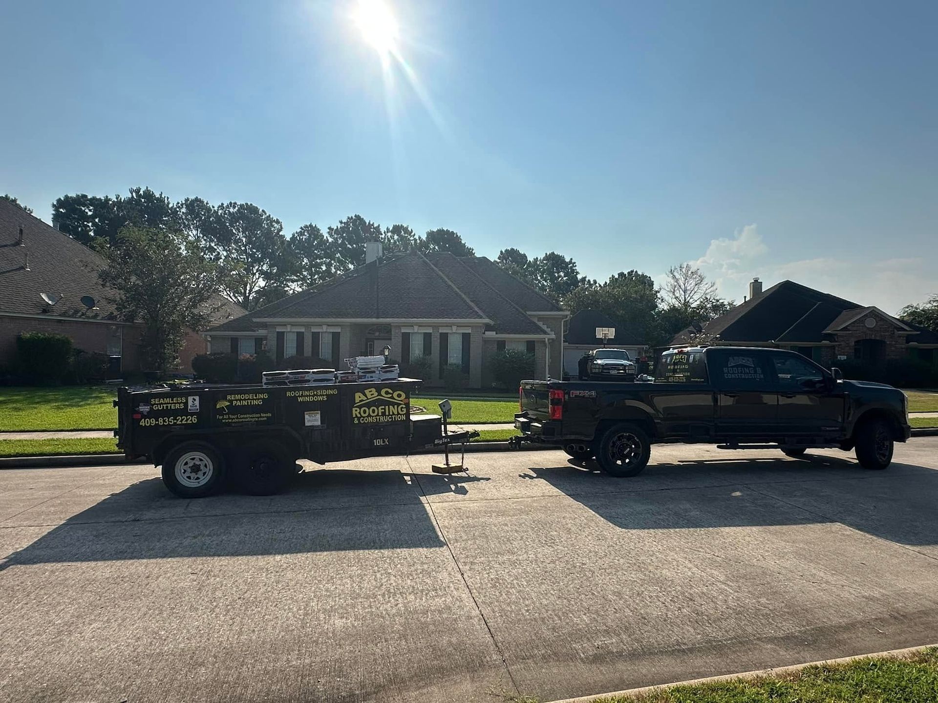 Two black trucks with trailers parked on a sunny suburban street