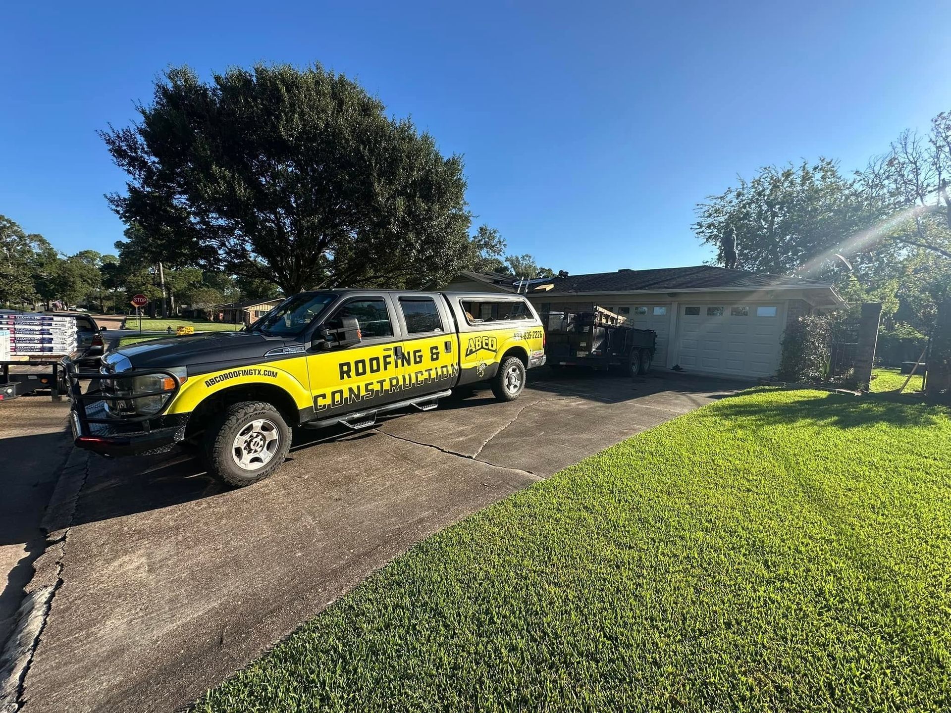 Yellow-and-black pickup truck parked in a driveway beside a house, with bright sun and green lawn