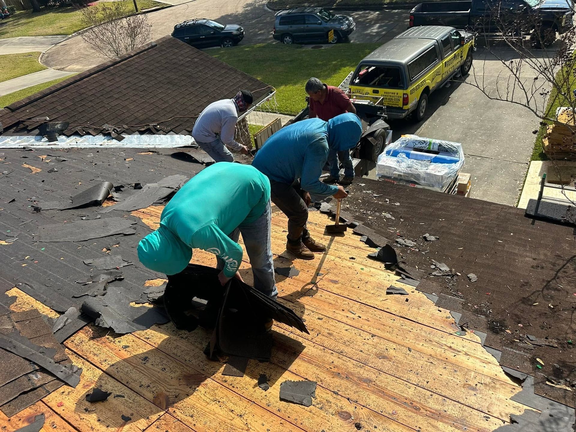 Workers repairing a shingled roof on a house, with tools and debris visible.