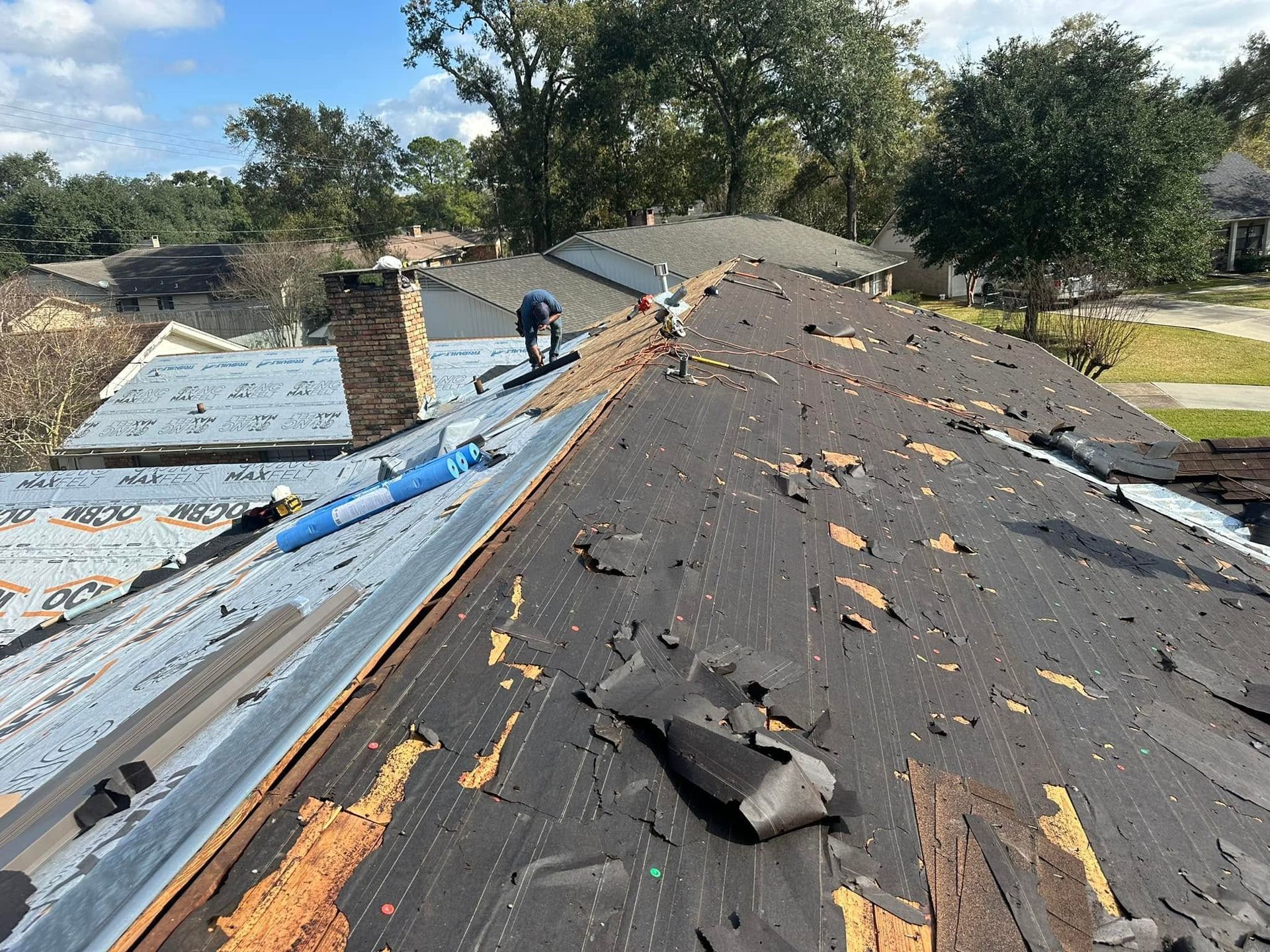 Roofer repairing a damaged shingle roof with exposed blue underlayment and debris after storm damage