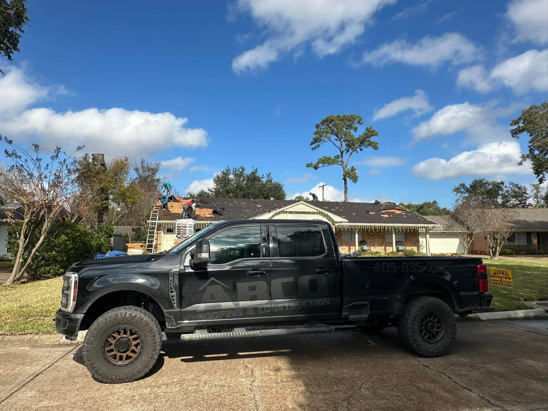 Black lifted pickup truck parked on a lawn in front of houses under a blue sky with clouds