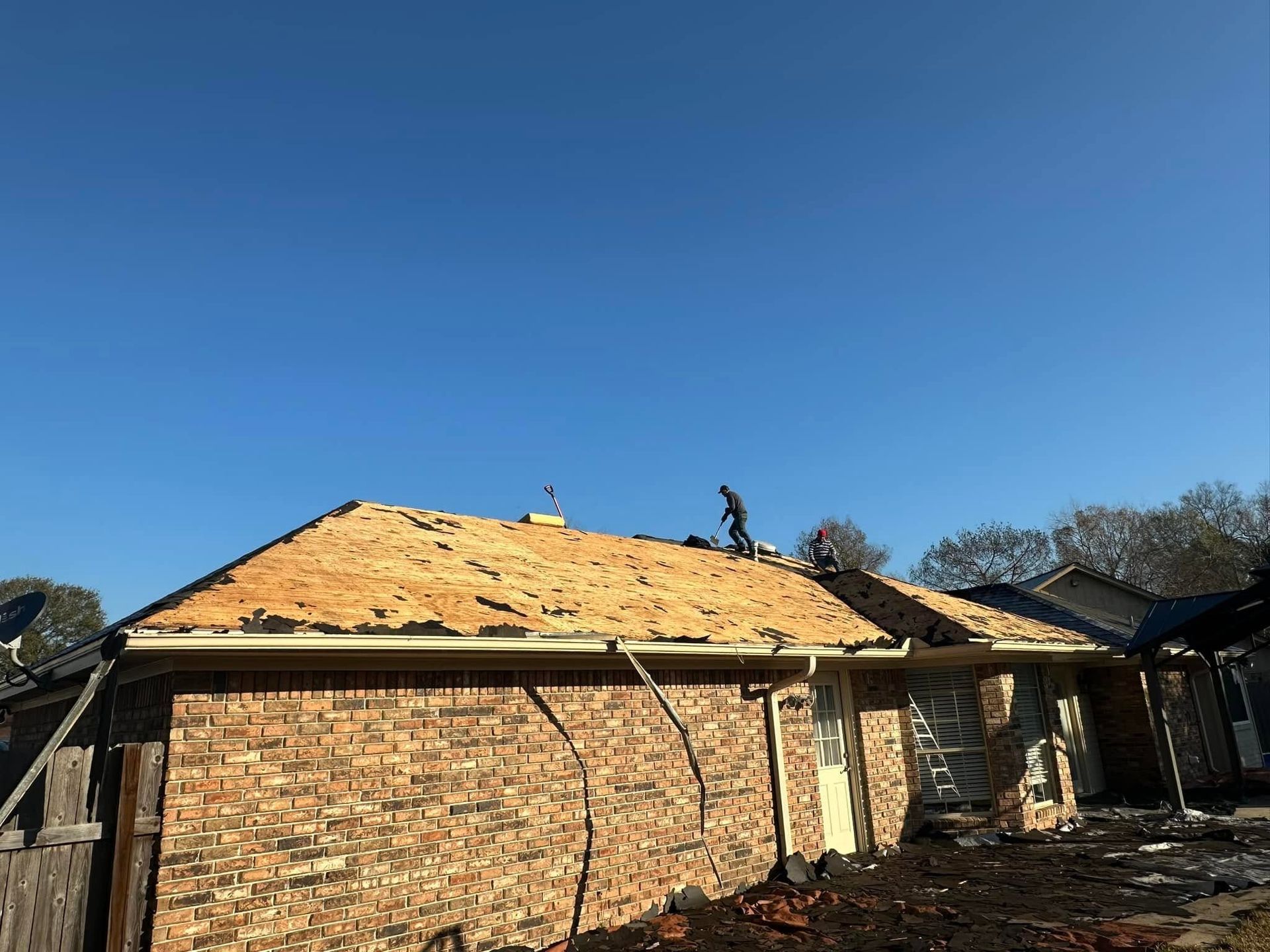 Unfinished brick house with workers on the roof under a clear blue sky