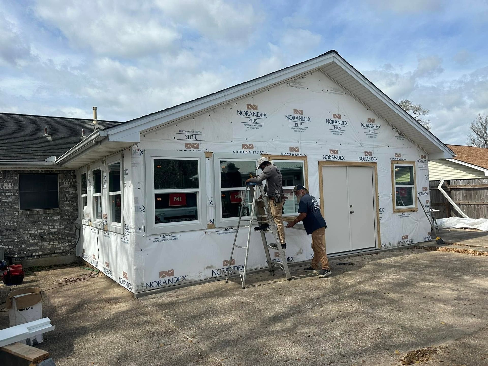 Workers installing siding on a white house addition under construction