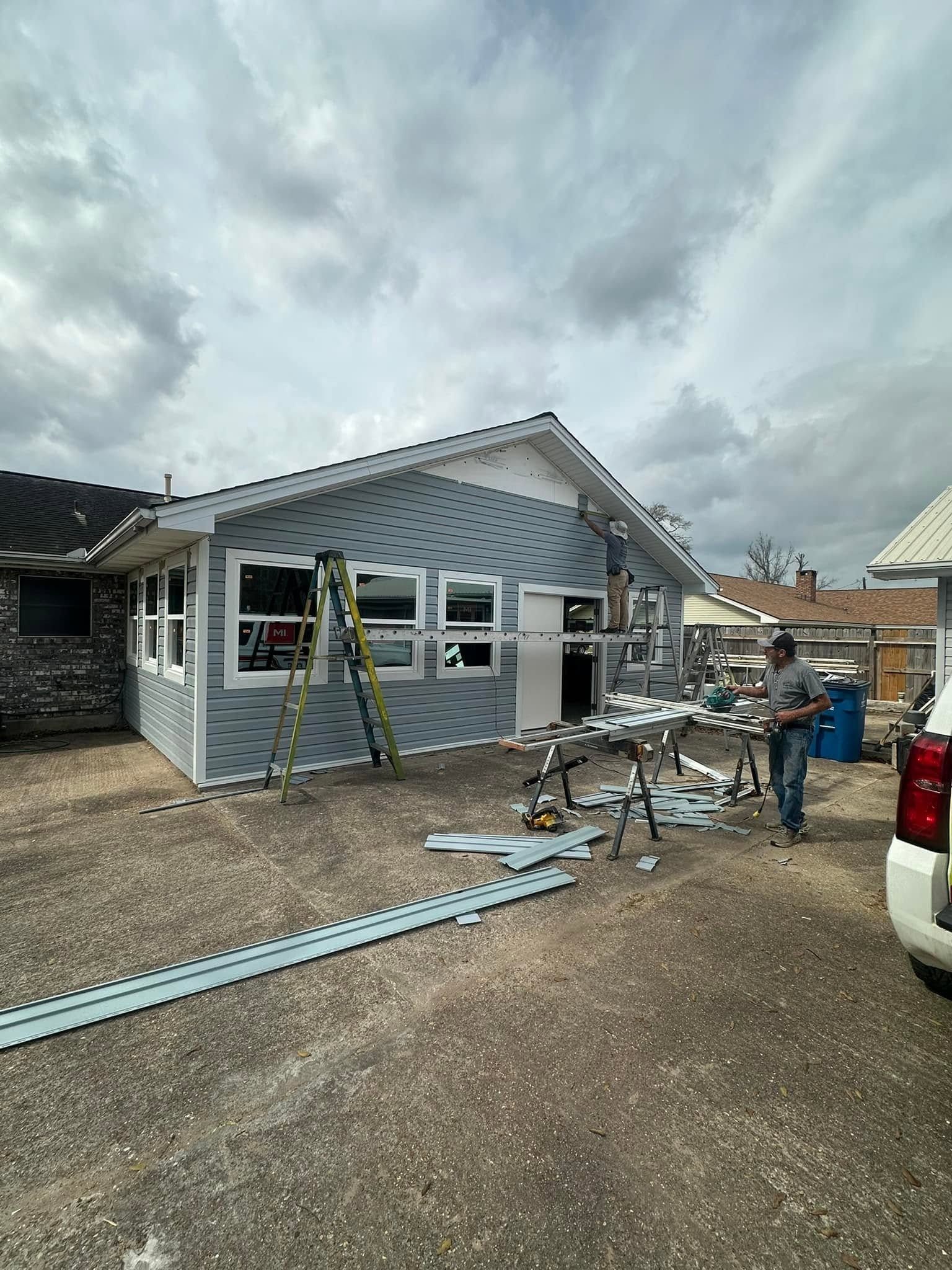 Partially built house exterior with workers’ tools, ladders, and siding materials on a gravel driveway.