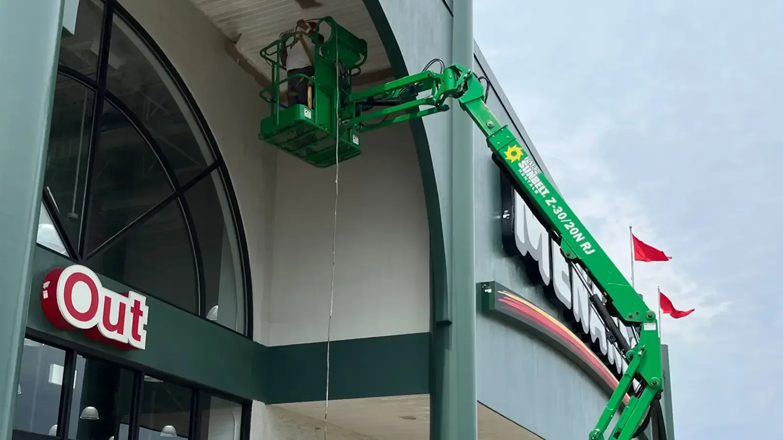 Person in green lift working on a building sign. Bright green lift and building, blue sky.