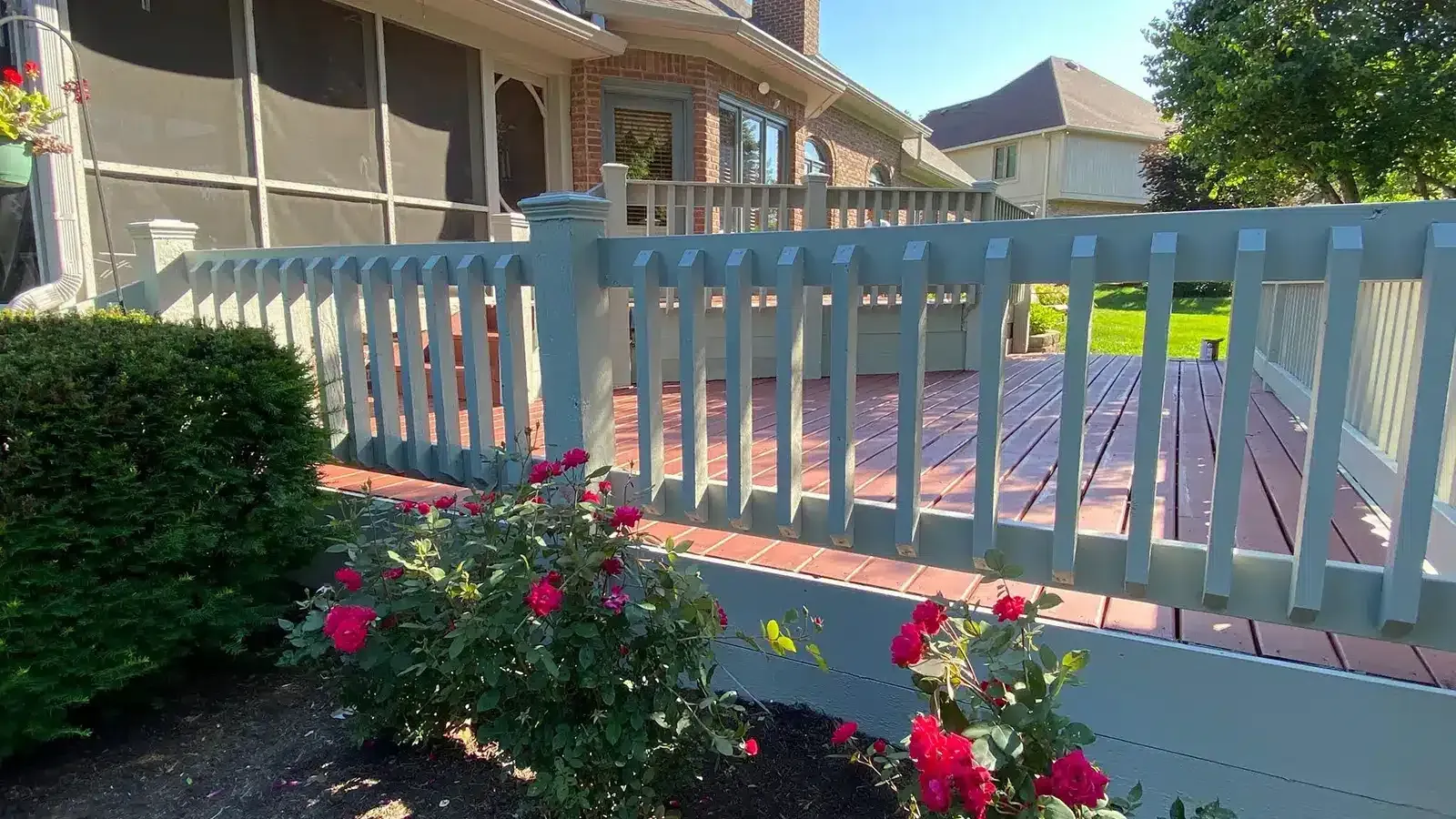 Green deck with red roses in foreground, house in background.