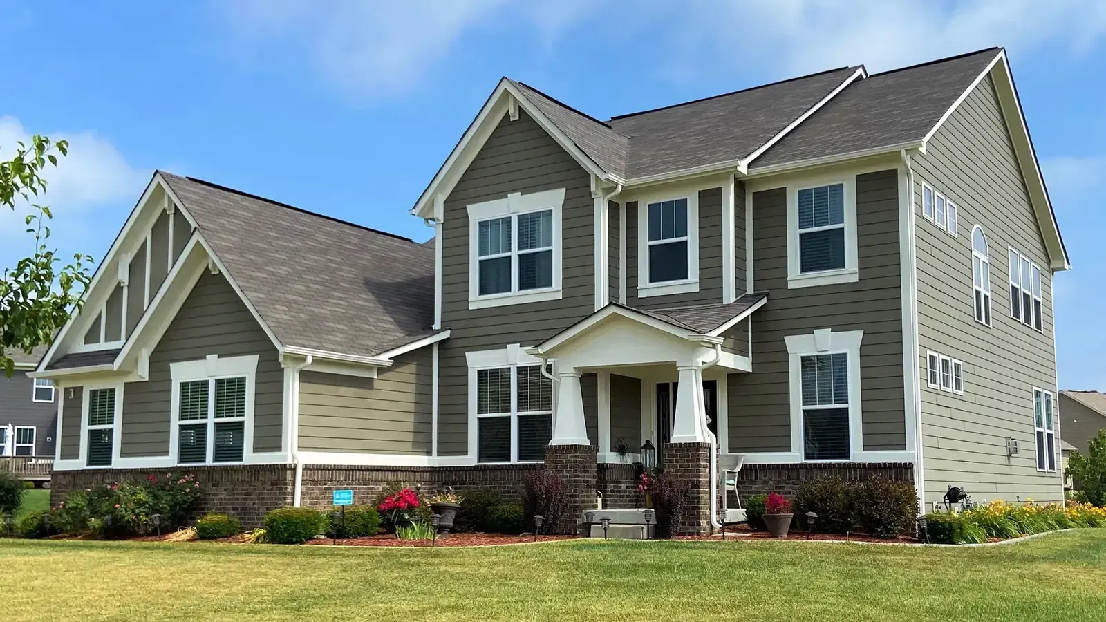 Two-story house with gray and brown siding, white trim, and a blue sky.