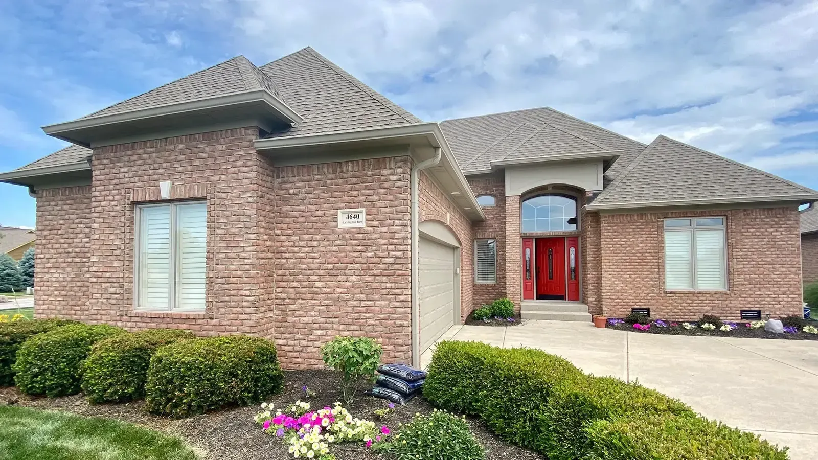 Brick house with a red door, landscaping, and a driveway.