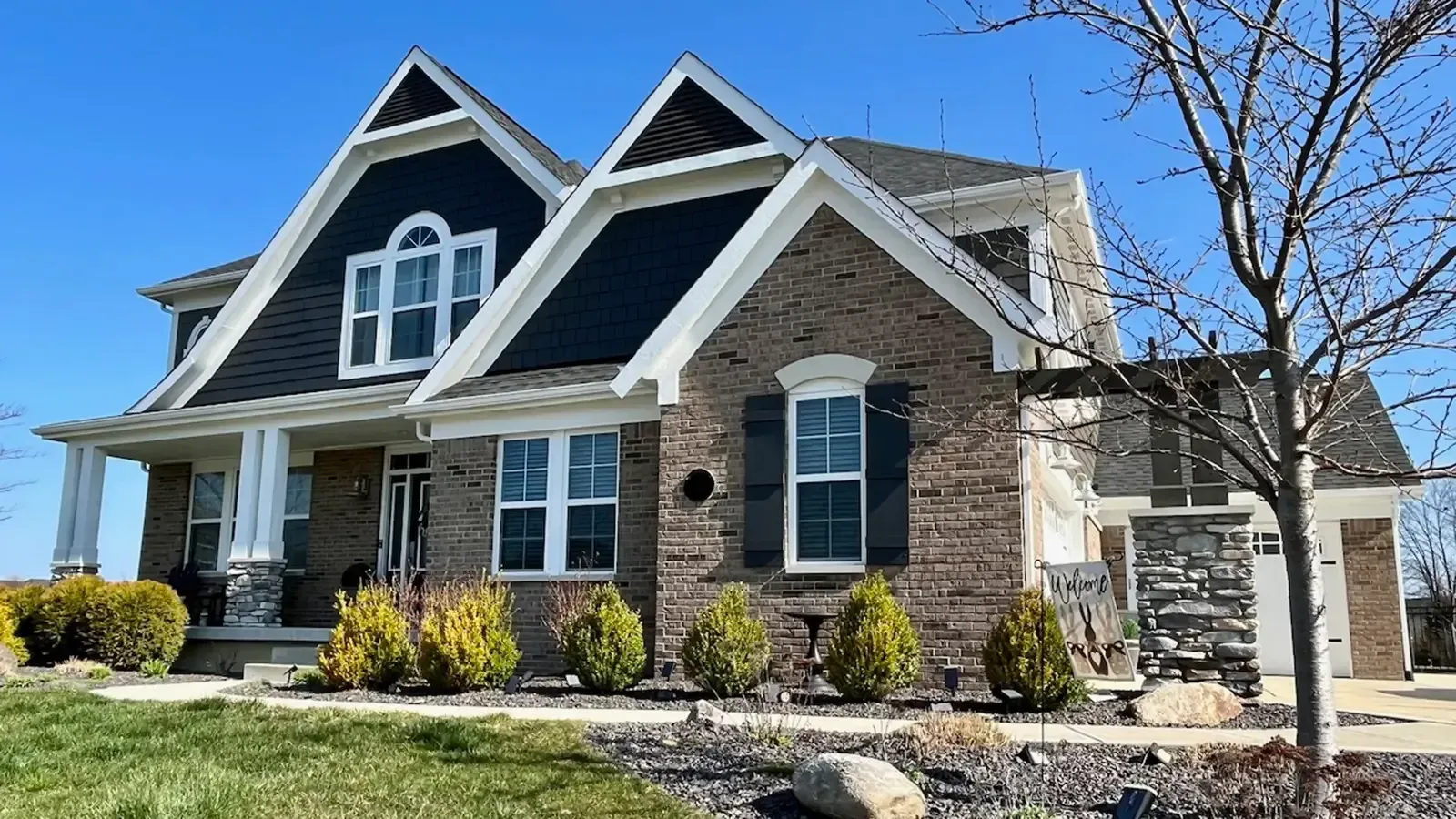 Two-story brick house with black roof gables, white trim, and blue sky.