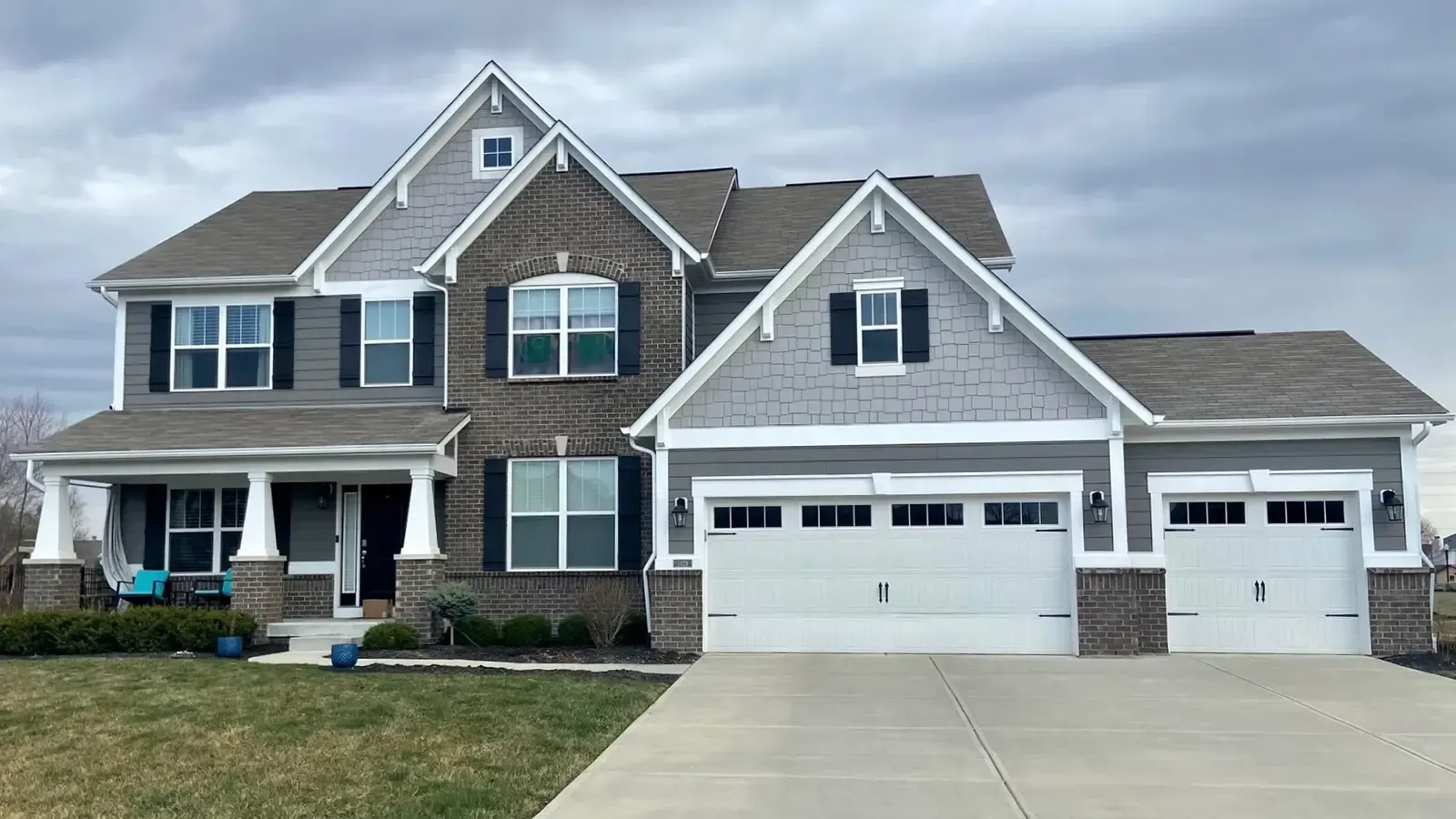 Two-story house with gray siding, brick, and three-car garage under a cloudy sky.