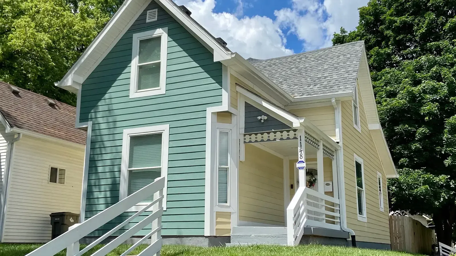 Two-story house, blue and yellow siding, white trim, porch, stairs, green lawn, sunny day.