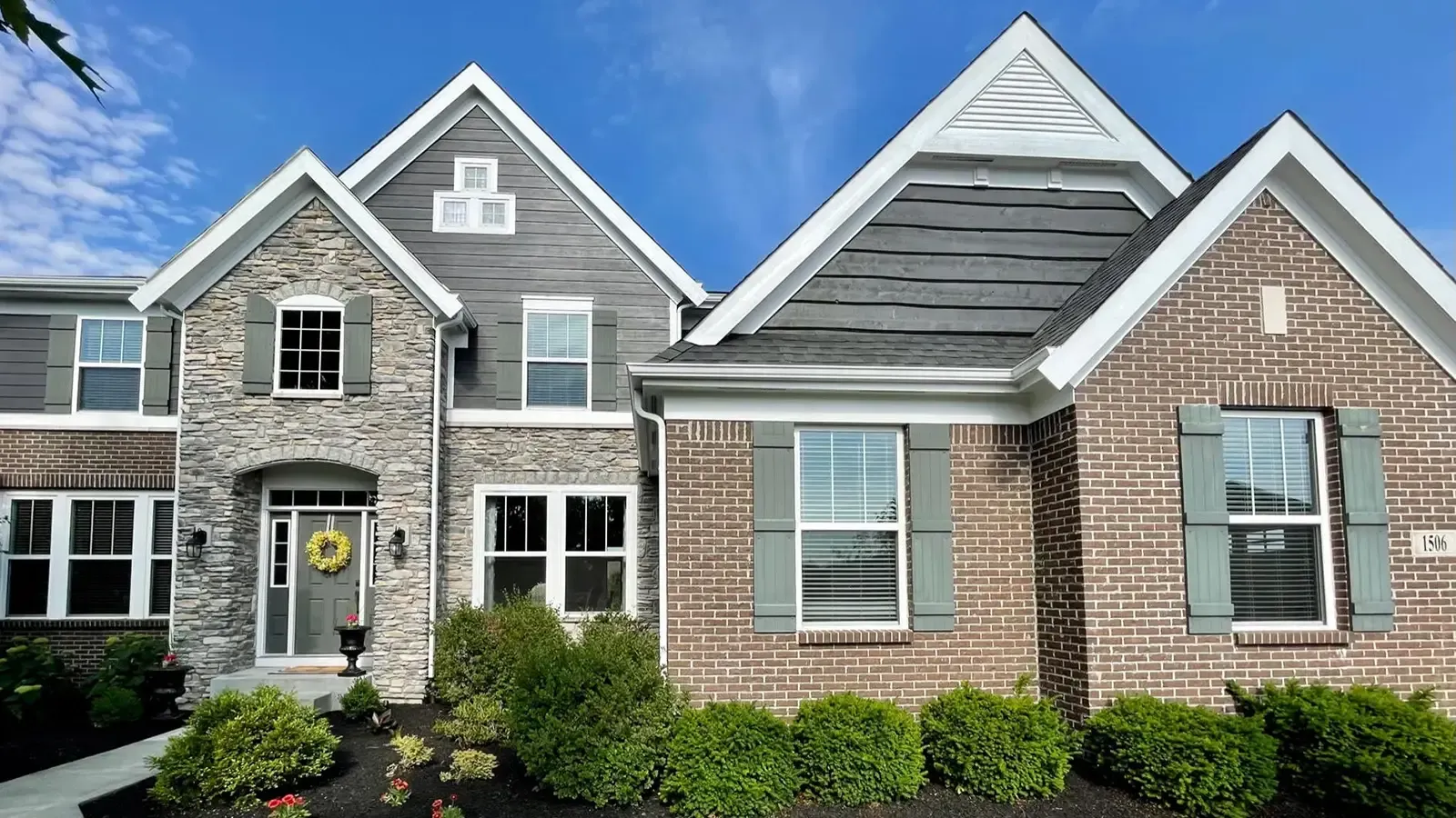 Two-story brick and stone home with gray shutters and a blue sky.