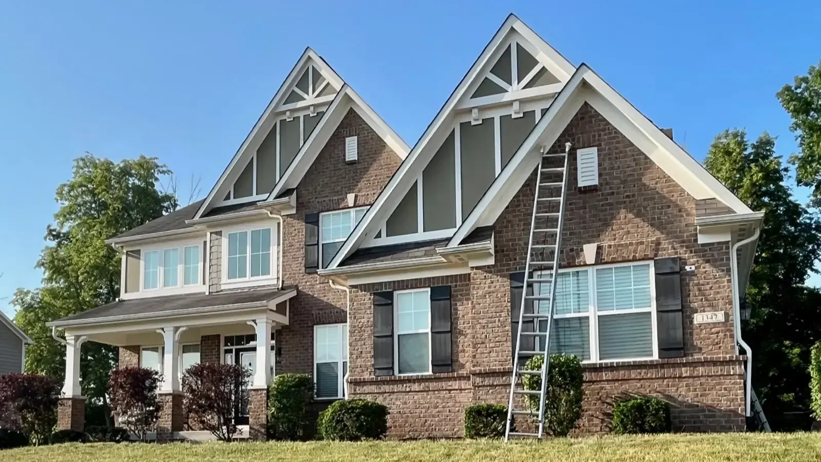 Two-story brick house with a ladder against the side, blue sky.