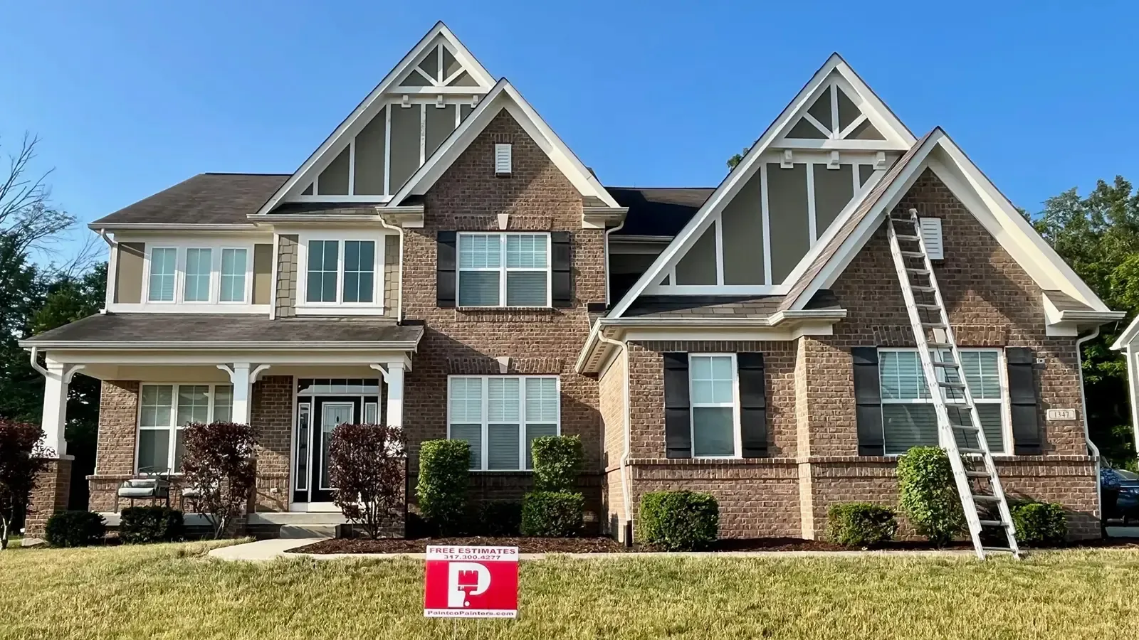 Two-story brick house with ladder. Beige trim, dark roof, black shutters. Red sign in the grass.