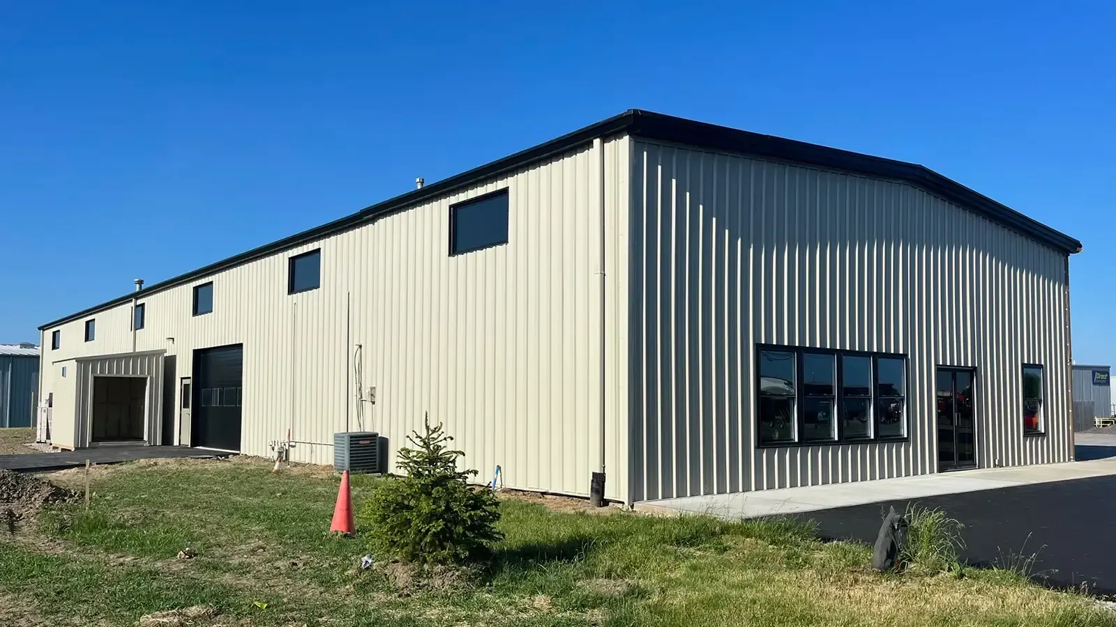 Cream-colored industrial building with black trim and windows against a clear blue sky.