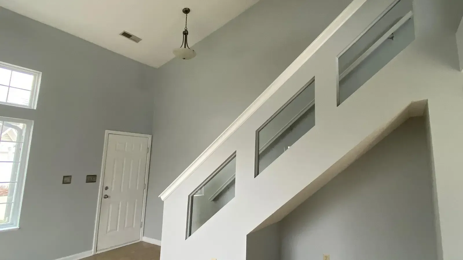Interior view of a house with gray walls, a white railing, and a door.