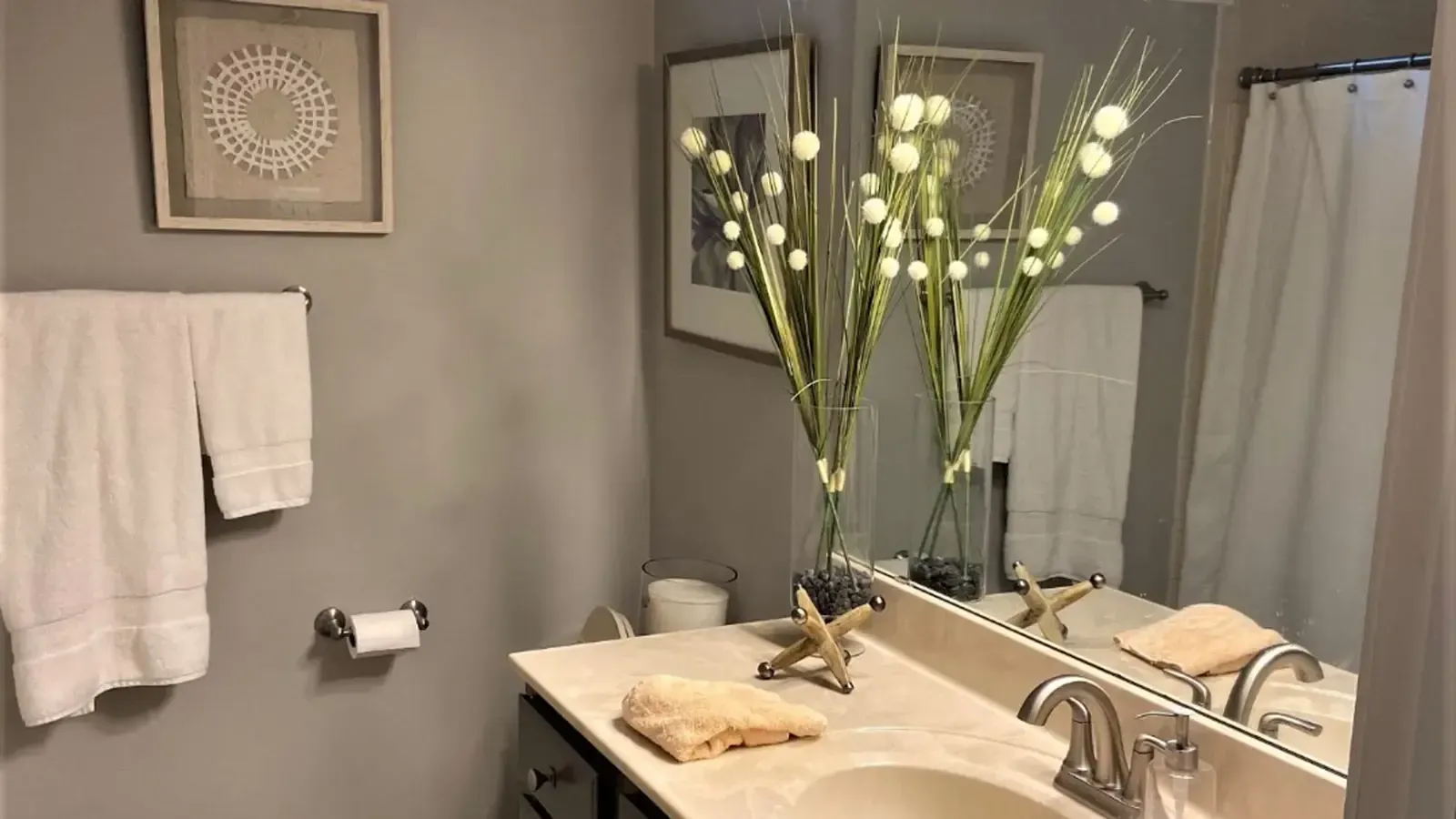 Bathroom with white towels, decorations, and a mirror reflecting light.