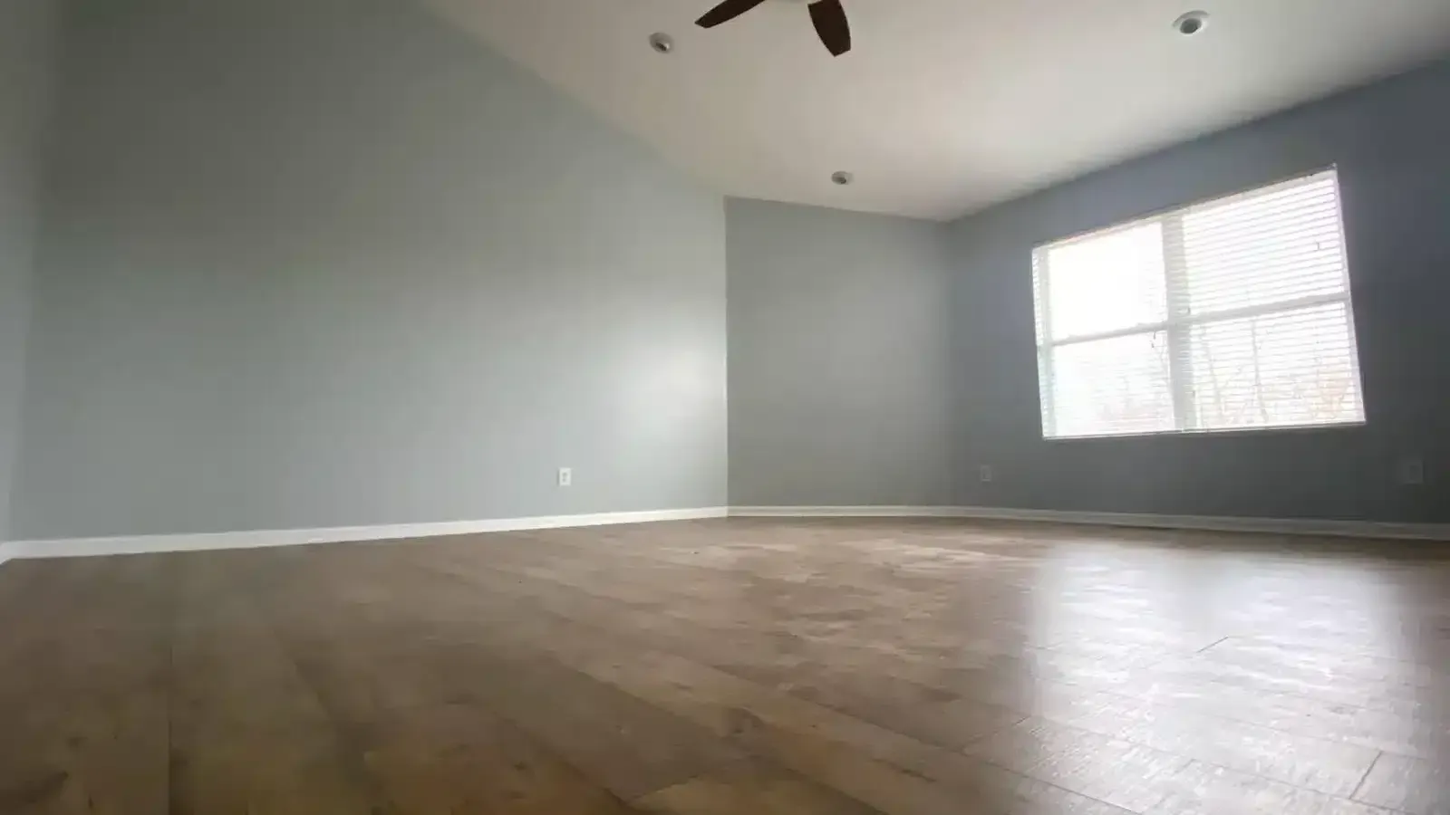 Empty room with wood-look flooring, light blue walls, a window, and a vaulted ceiling.