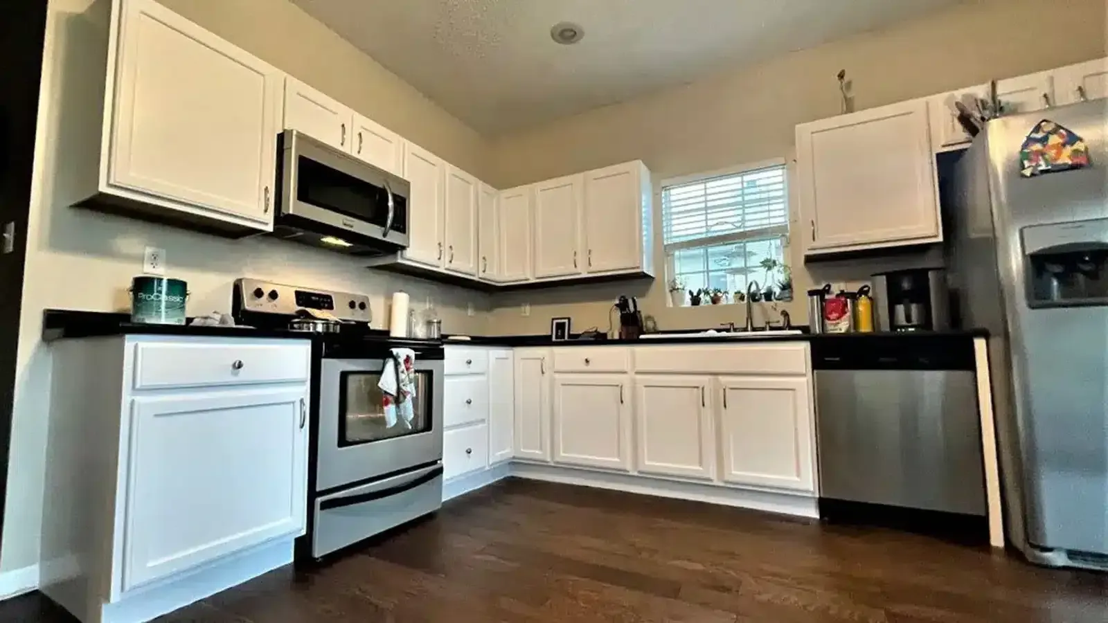 White kitchen with stainless steel appliances, black countertops, and dark wood floor.