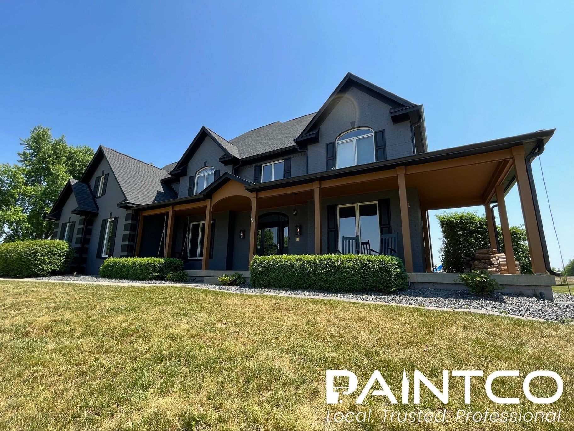 Dark gray house with brown porch roof and trim, on a green lawn under blue sky.