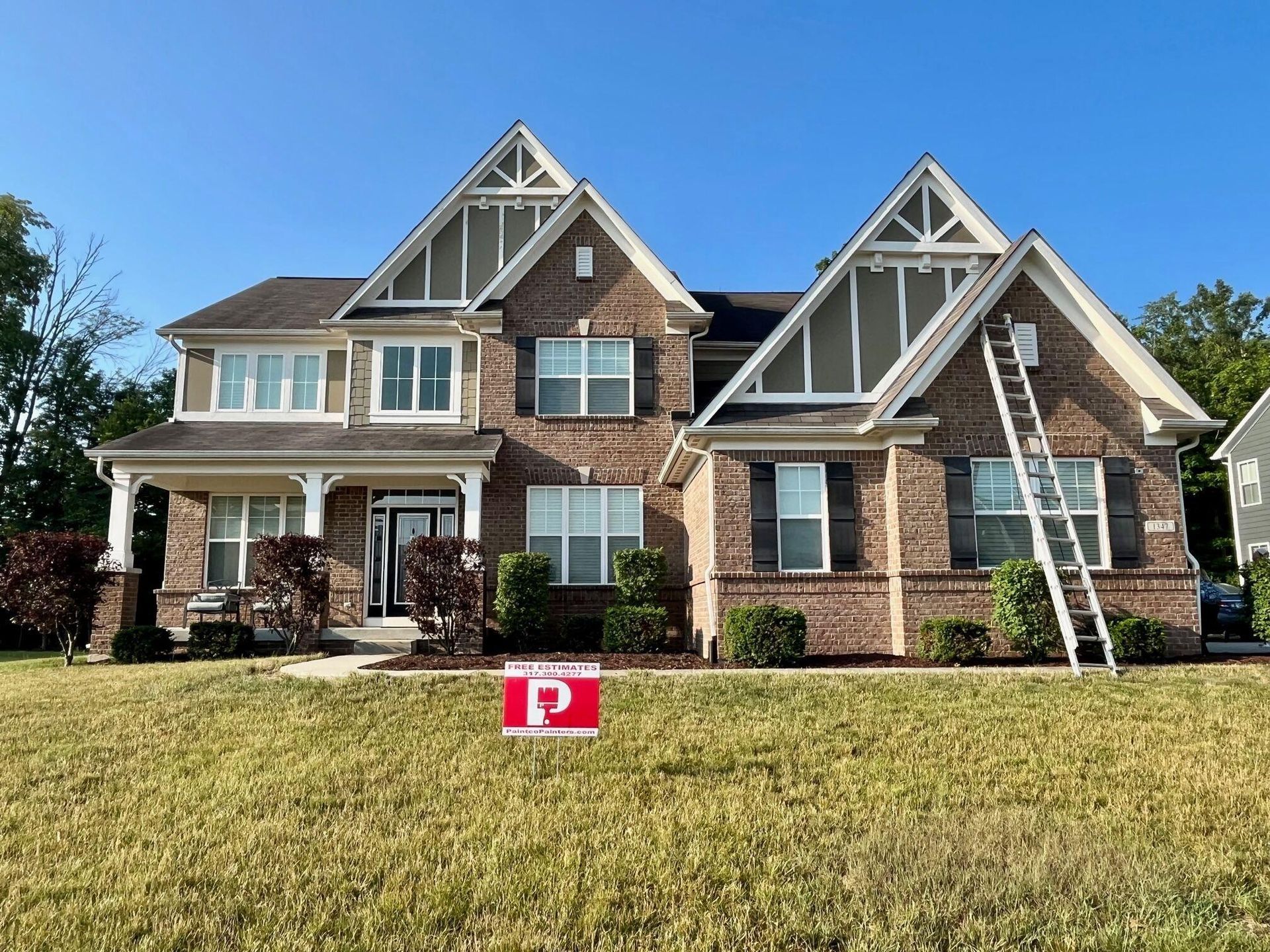 Two-story brick house with ladder against the roof, yard, and a red sign.