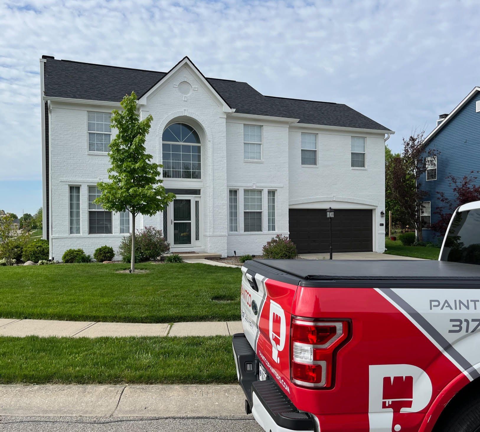 White house with black roof, red and white truck parked in front.