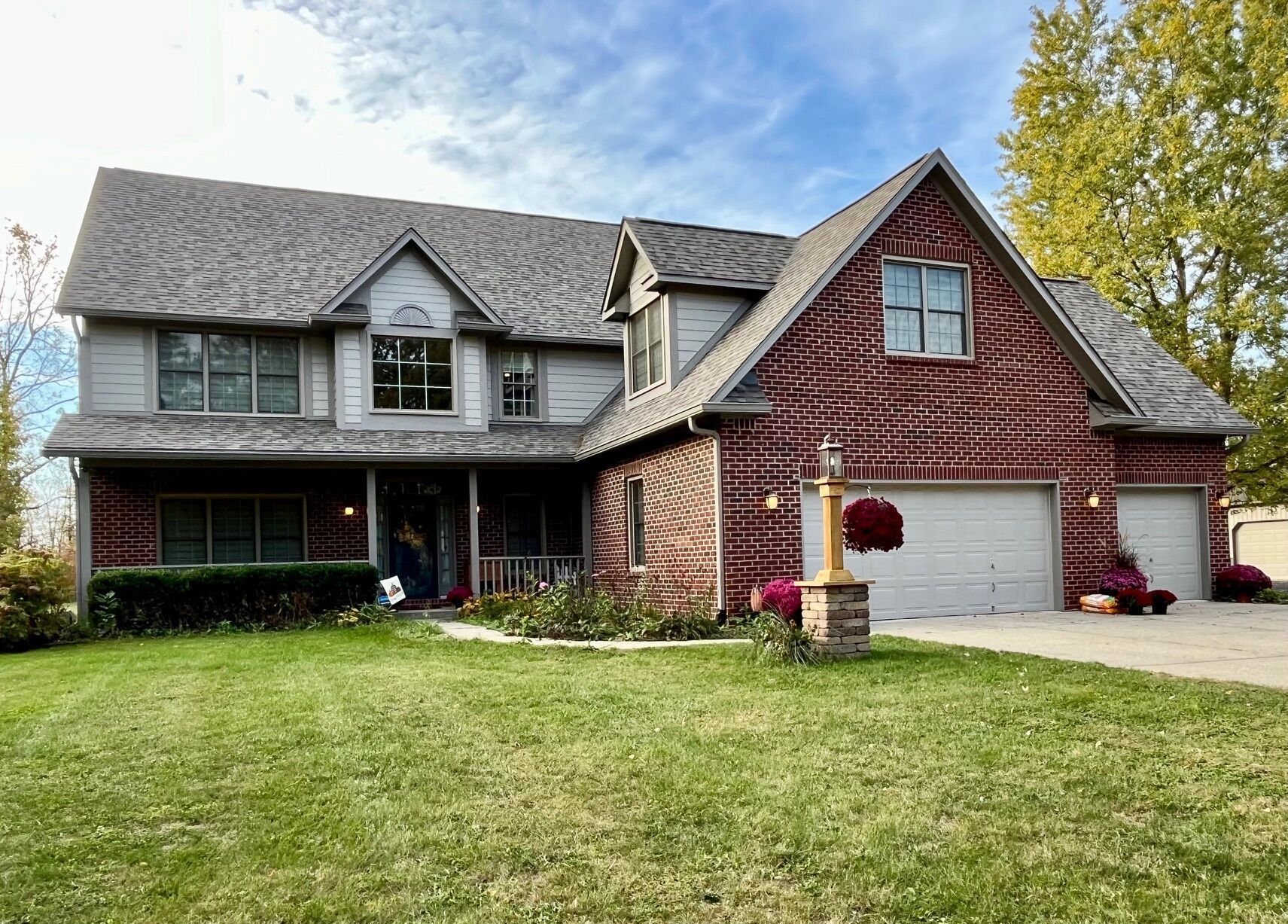 Two-story brick house with a green lawn and a cloudy sky. Features a porch and a three-car garage.
