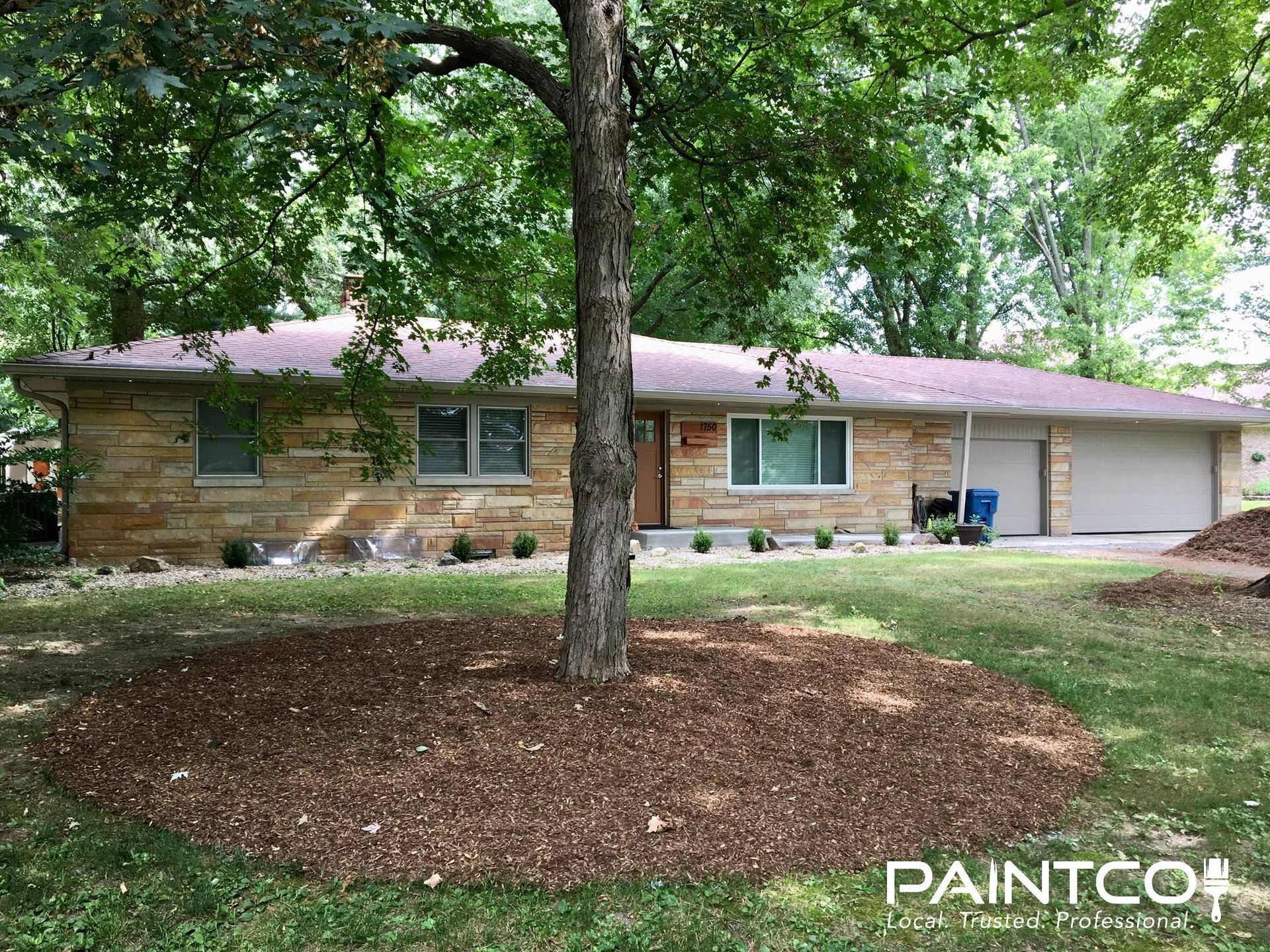 Ranch house with stone facade and mulch around a tree in the yard.