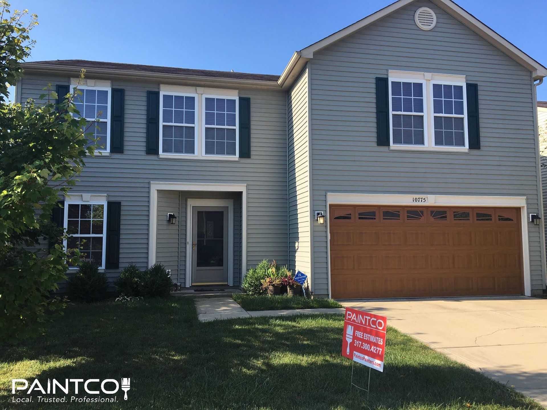 Two-story house with blue siding, green shutters, and a brown garage door, with a 
