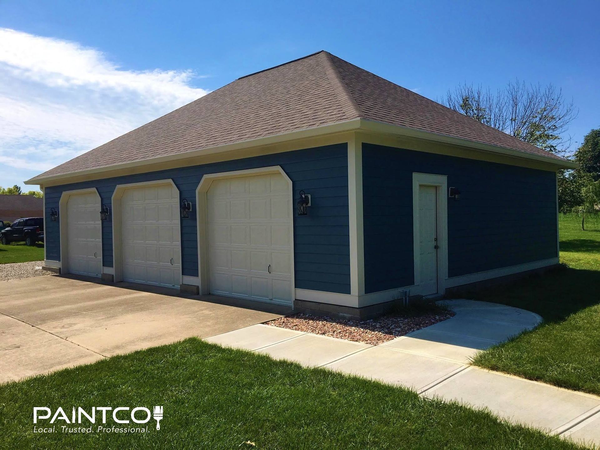 Blue three-car garage with tan trim and doors; concrete driveway and walkway; green lawn.