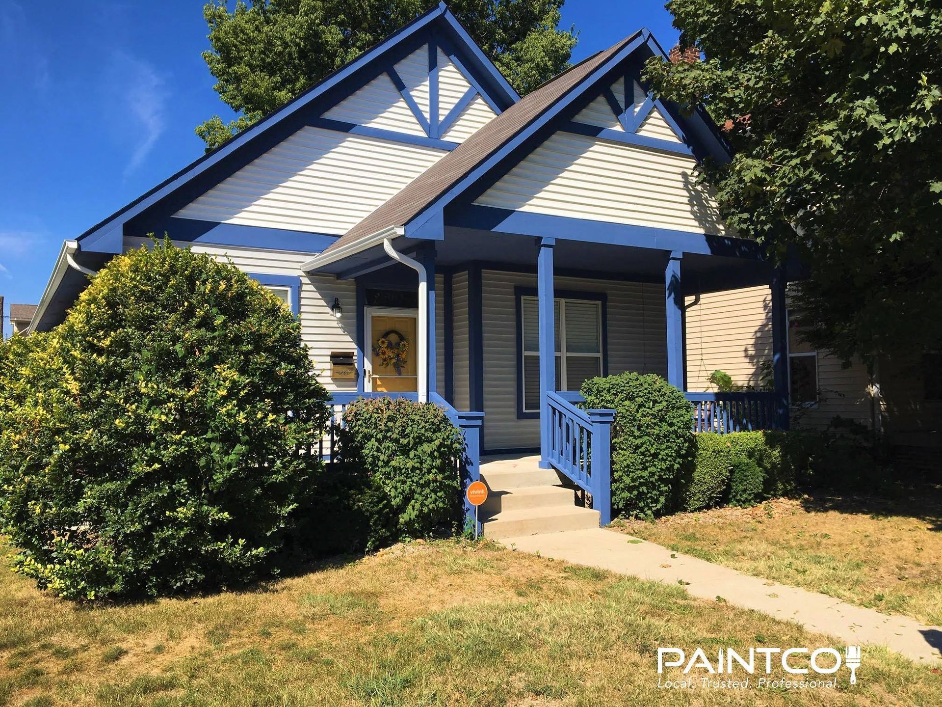 Cottage with blue trim, a porch, and a yellow door on a sunny day.