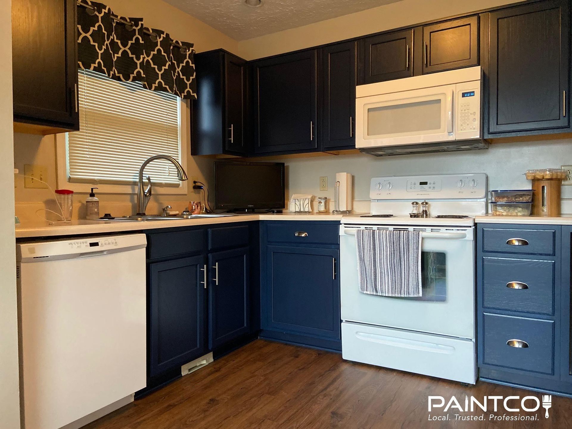 Kitchen with dark blue cabinets, white appliances, and a wood floor.
