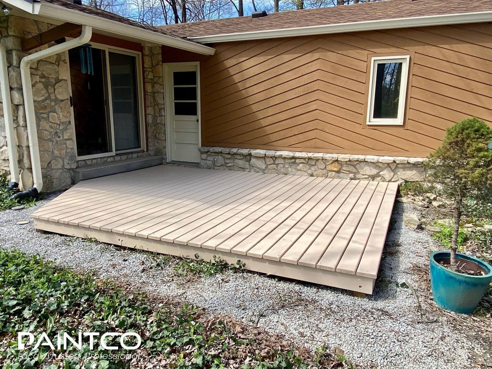 A composite deck, tan siding and natural stone foundation of a home.