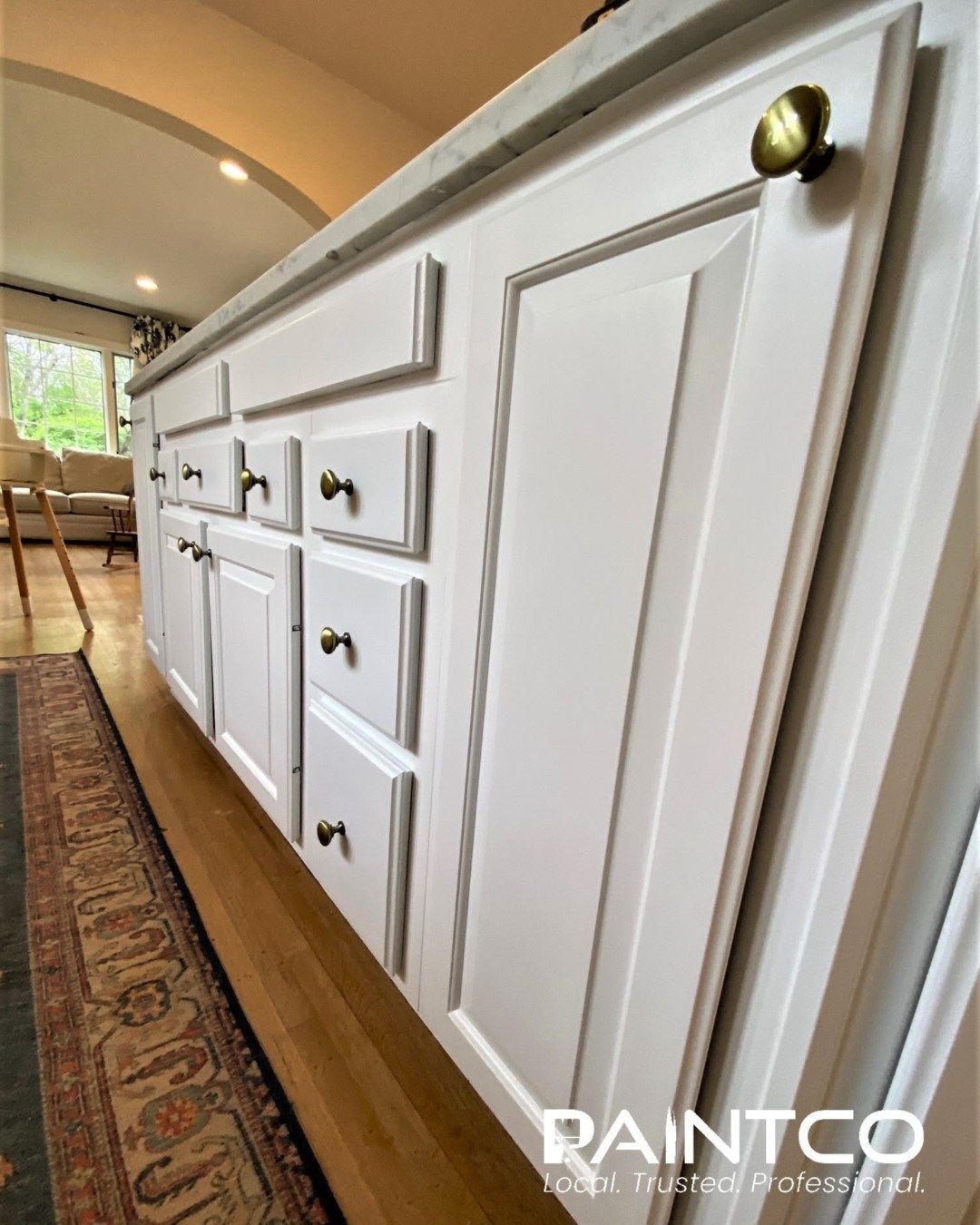 White kitchen island with gold knobs and gray countertop.