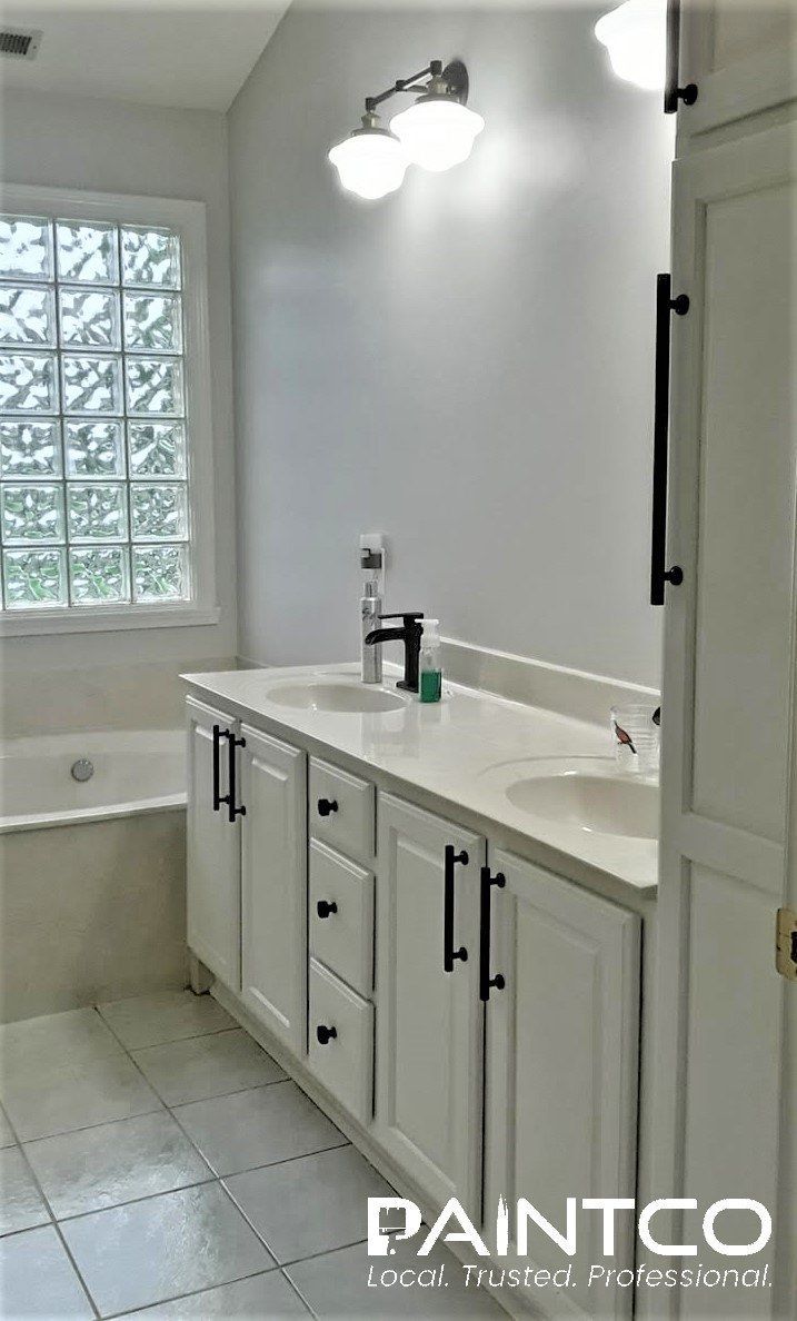 Bathroom with white cabinets, light gray walls, glass block window, and white countertops.
